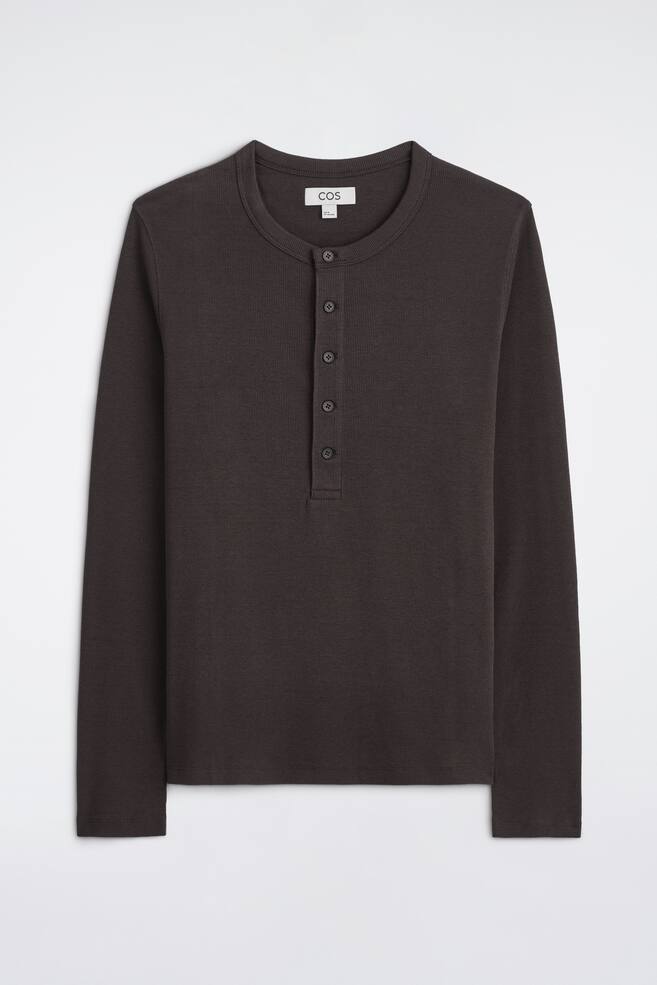 En smal, ribbstickad lÃ¥ngÃ¤rmad Henley-t-shirt i mÃ¶rkbrunt ligger platt och visas framifrÃ¥n. Den har rund halsringning, en knappslÃ¥ med fem knappar framtill och lÃ¥nga Ã¤rmar med en fin ribbad struktur Ã¶ver hela plagget. - 1