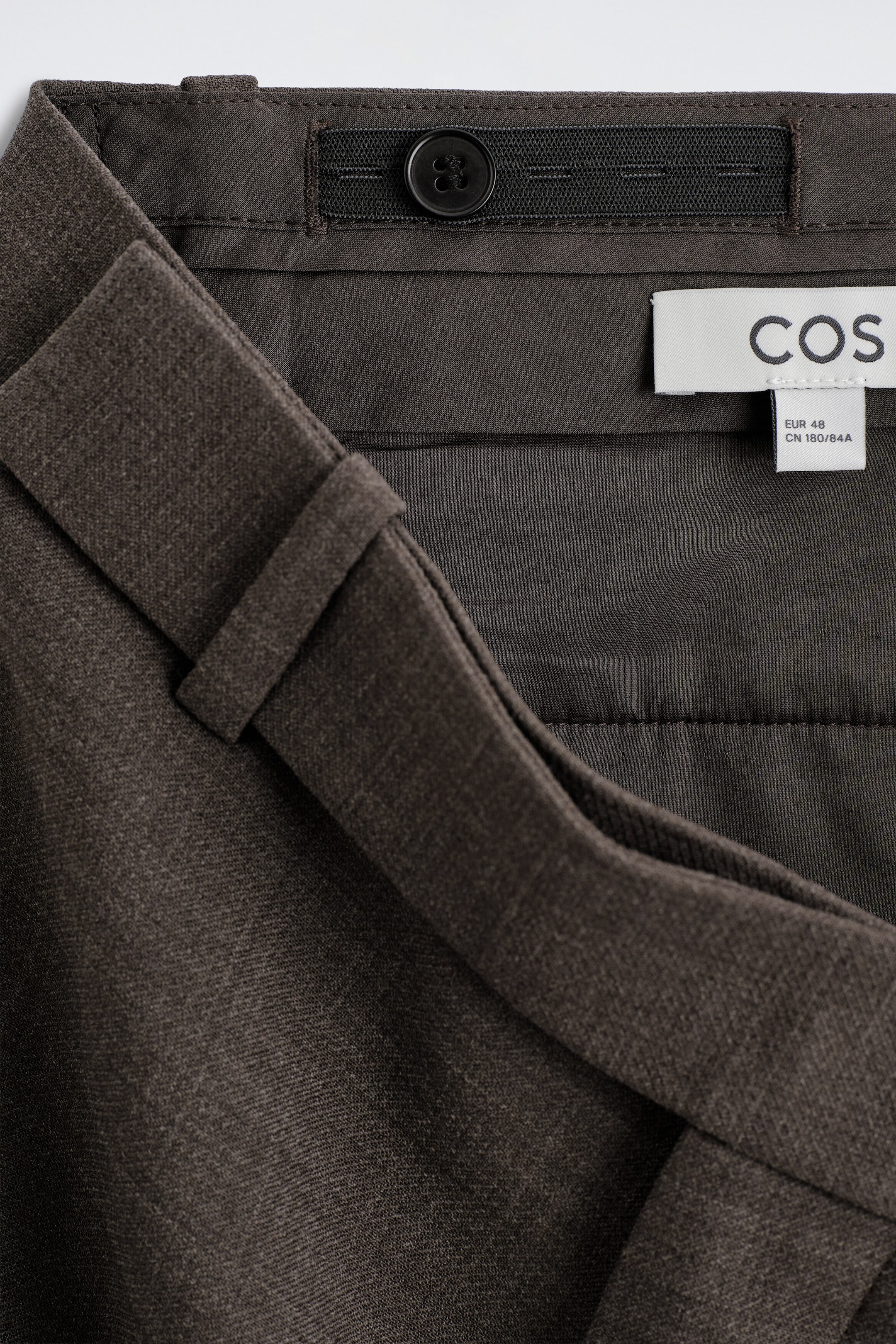 This close-up shot of the wool-blend relaxed-fit straight-leg trousers shows the inner waistband detail, featuring an adjustable elastic band with a black button and a white brand label. The exterior shows a textured dark brown fabric and a structured belt loop. This close-up shot of the wool-blend relaxed-fit straight-leg trousers shows the inner waistband detail, featuring an adjustable elastic band with a black button and a white brand label. The exterior shows a textured dark brown fabric and a structured belt loop.