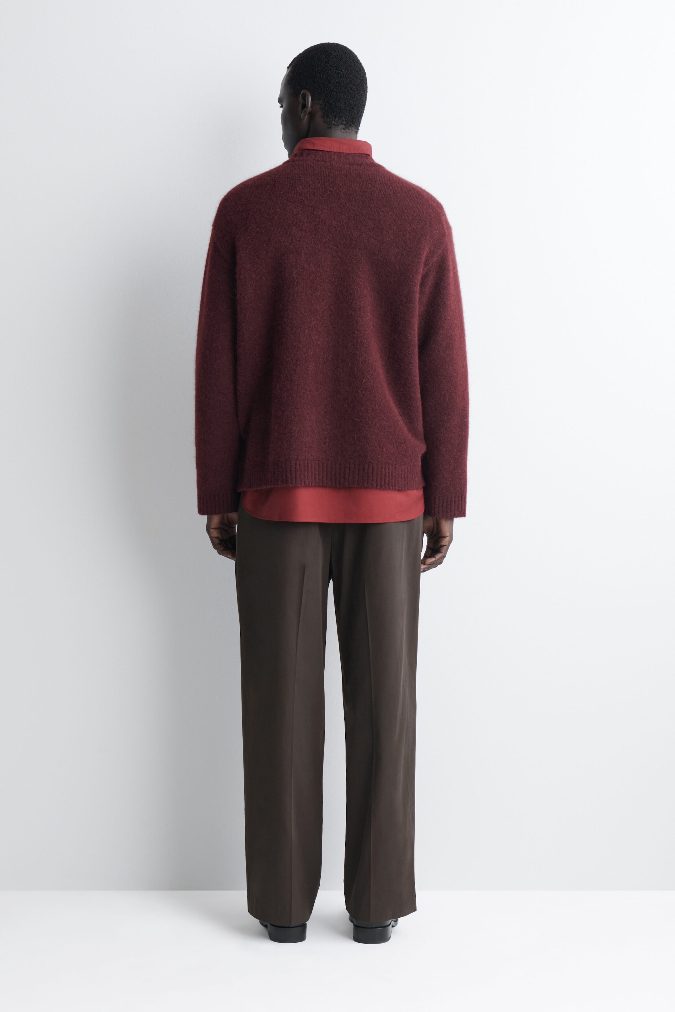 The oversized alpaca-blend crew-neck jumper in burgundy is shown from the back, highlighting its relaxed fit, dropped shoulders, and ribbed hem and cuffs. The jumper is layered over a red collared shirt, with the collar and bottom hem extending past the knitwear. The oversized alpaca-blend crew-neck jumper in burgundy is shown from the back, highlighting its relaxed fit, dropped shoulders, and ribbed hem and cuffs. The jumper is layered over a red collared shirt, with the collar and bottom hem extending past the knitwear.