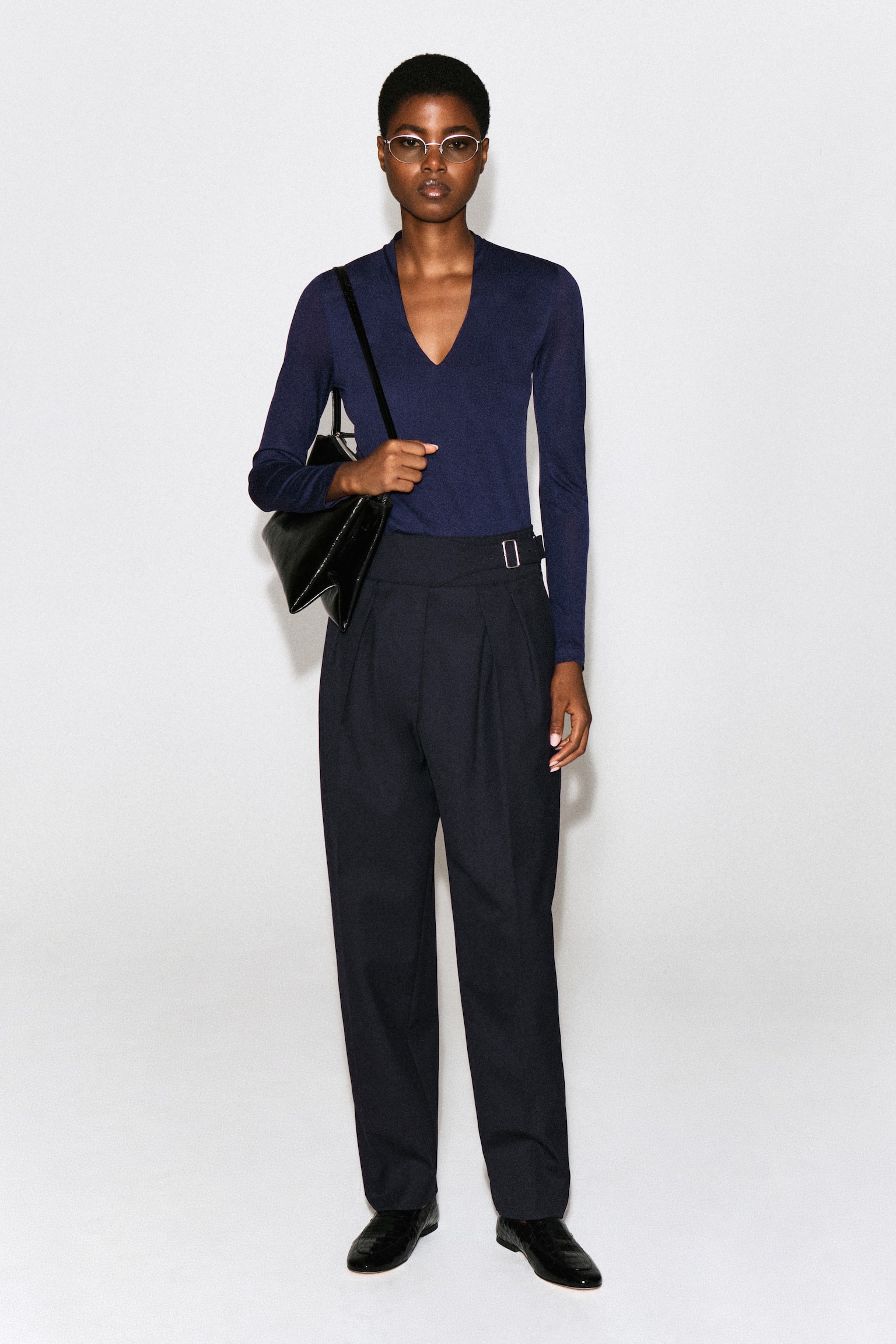 Een marineblauwe top met lange mouwen wordt van voren getoond en heeft een slim-fit silhouet en een diepe V-hals. De top is ontworpen met een licht opstaande, gedrapeerde kraag aan de achterkant van de hals en een netjes afgewerkte zoom. - 1