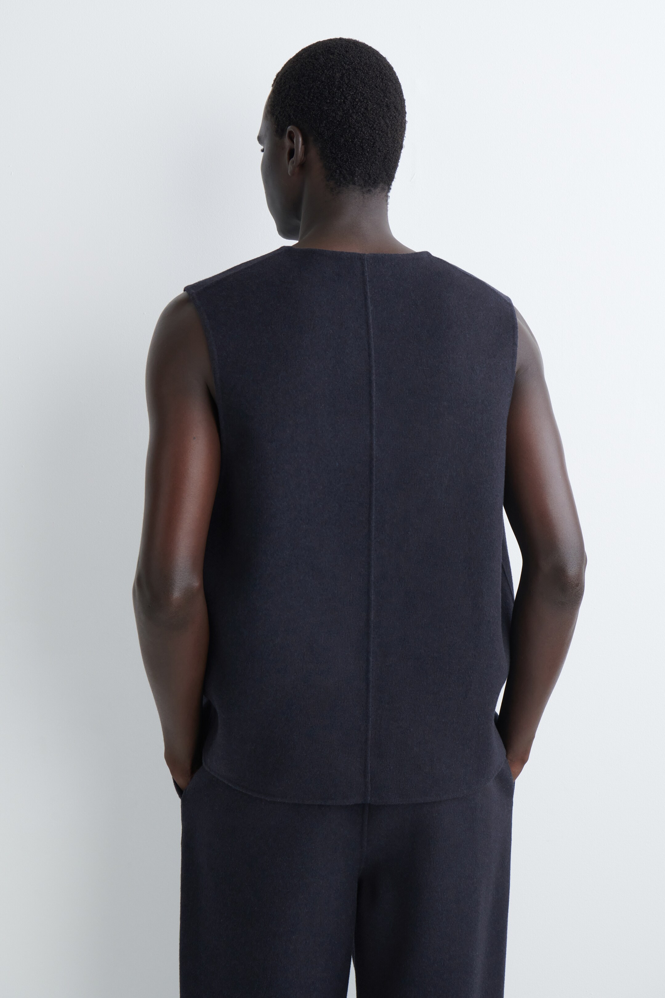 Agrandir l'image: Un haut sans manches bleu foncé à texture douce est présenté de dos. Il présente une couture verticale qui descend au centre du dos et un col ras du cou. Le haut est porté avec un pantalon bleu foncé assorti.