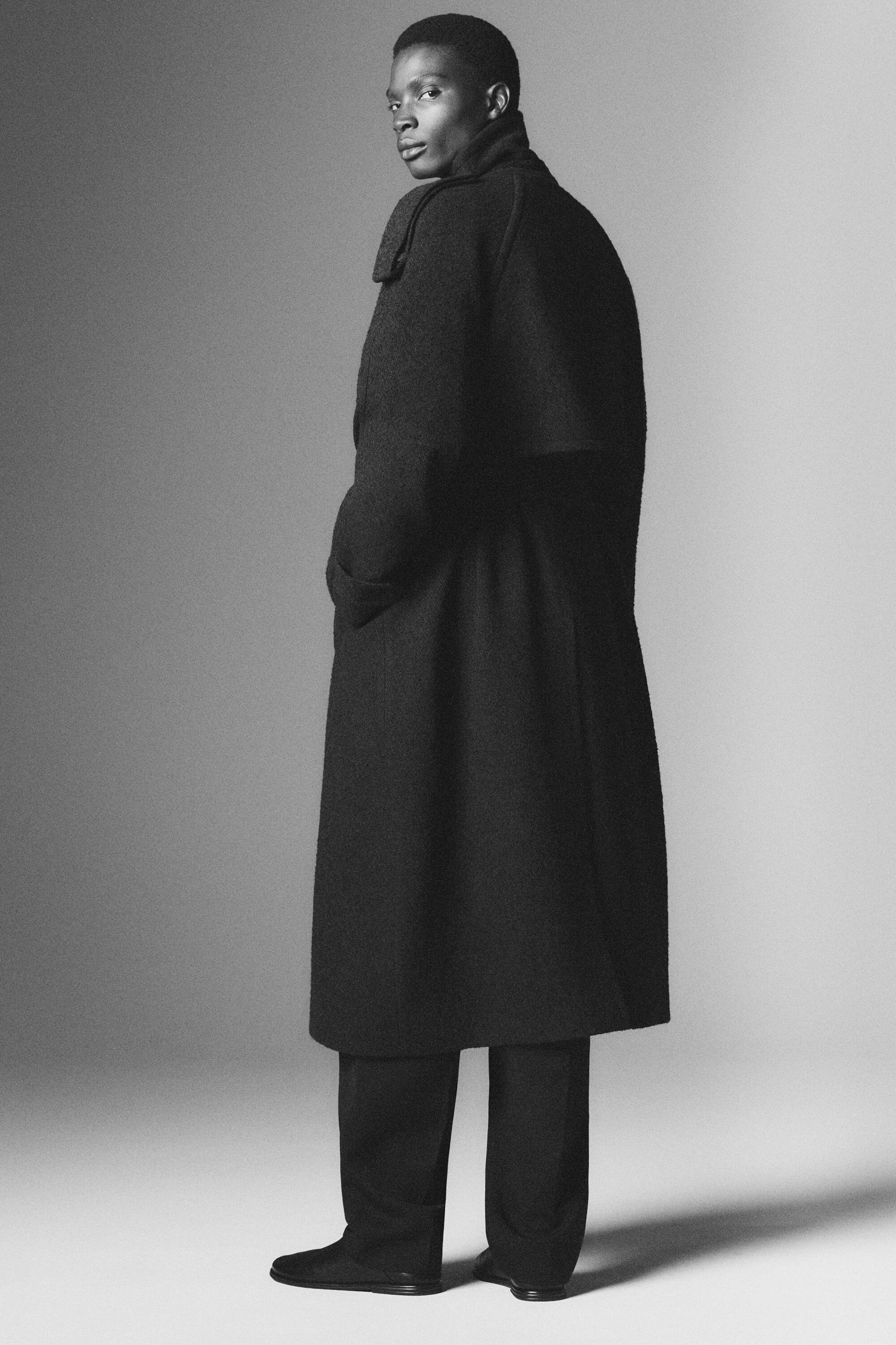 Ein langer, dunkler Trenchcoat aus Wollmischung ist in einer Rückansicht aus drei Vierteln zu sehen und zeigt seine entspannte Silhouette, eine Schulterpasse über dem oberen Rücken und einen hohen Kragen. Der Mantel reicht bis zur Mitte der Wade und wird mit einer passenden dunklen Hose getragen. Ein langer, dunkler Trenchcoat aus Wollmischung ist in einer Rückansicht aus drei Vierteln zu sehen und zeigt seine entspannte Silhouette, eine Schulterpasse über dem oberen Rücken und einen hohen Kragen. Der Mantel reicht bis zur Mitte der Wade und wird mit einer passenden dunklen Hose getragen.