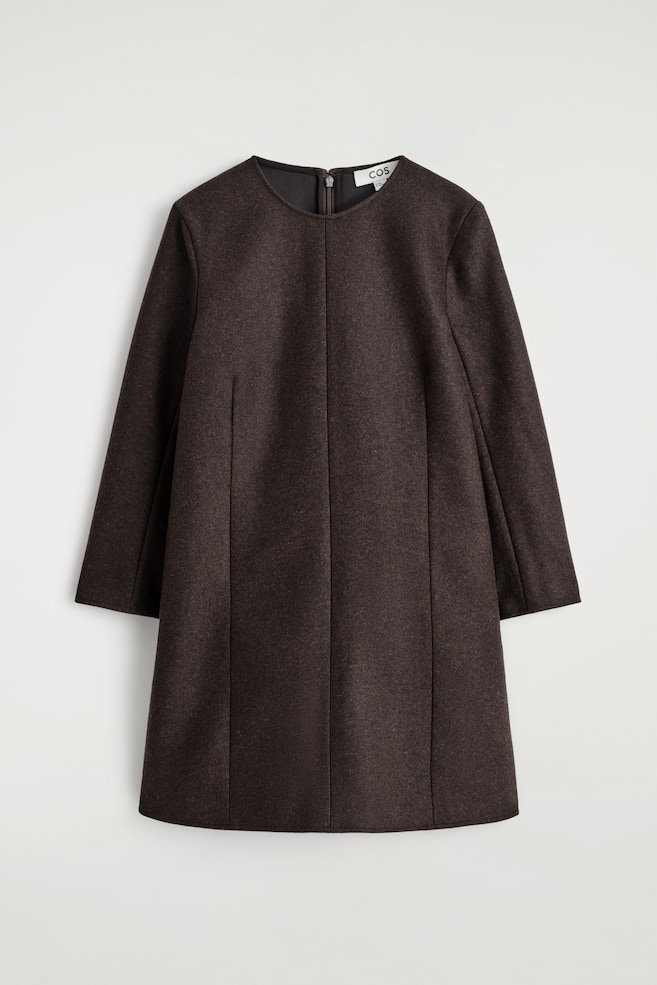 Un vestido mini marrón oscuro se presenta de frente, con un escote redondeado, mangas largas y dos costuras verticales con forma que recorren la parte delantera. Se ve un cierre de cremallera en la parte superior trasera del escote. - 1