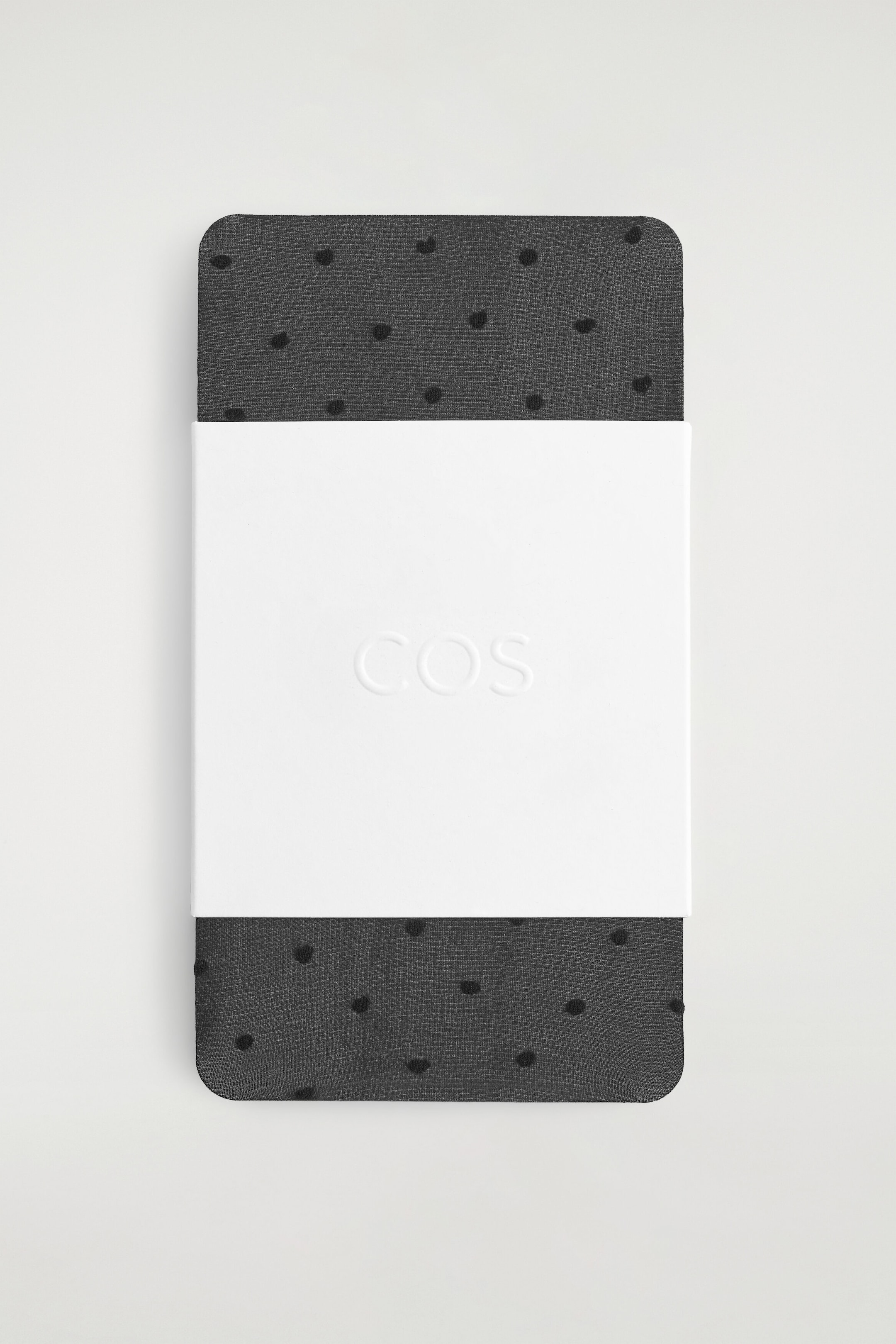 These sheer, dark grey socks featuring a black polka-dot jacquard pattern are shown folded flat, with a wide white paper band embossed with a logo wrapped around the centre.