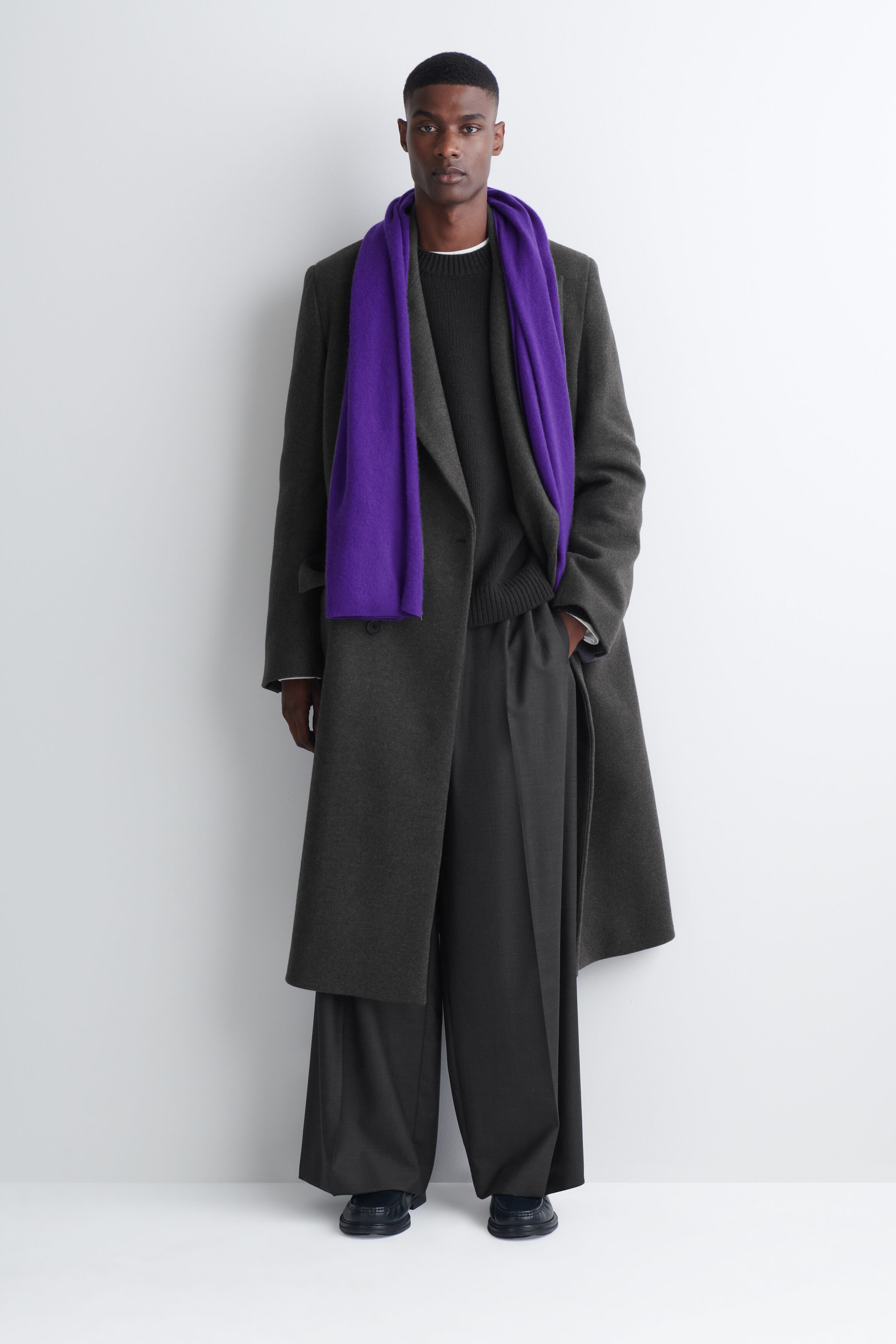 A purple cashmere scarf is being worn draped around the model's neck, hanging down the front of a dark gray overcoat. A purple cashmere scarf is being worn draped around the model's neck, hanging down the front of a dark gray overcoat.