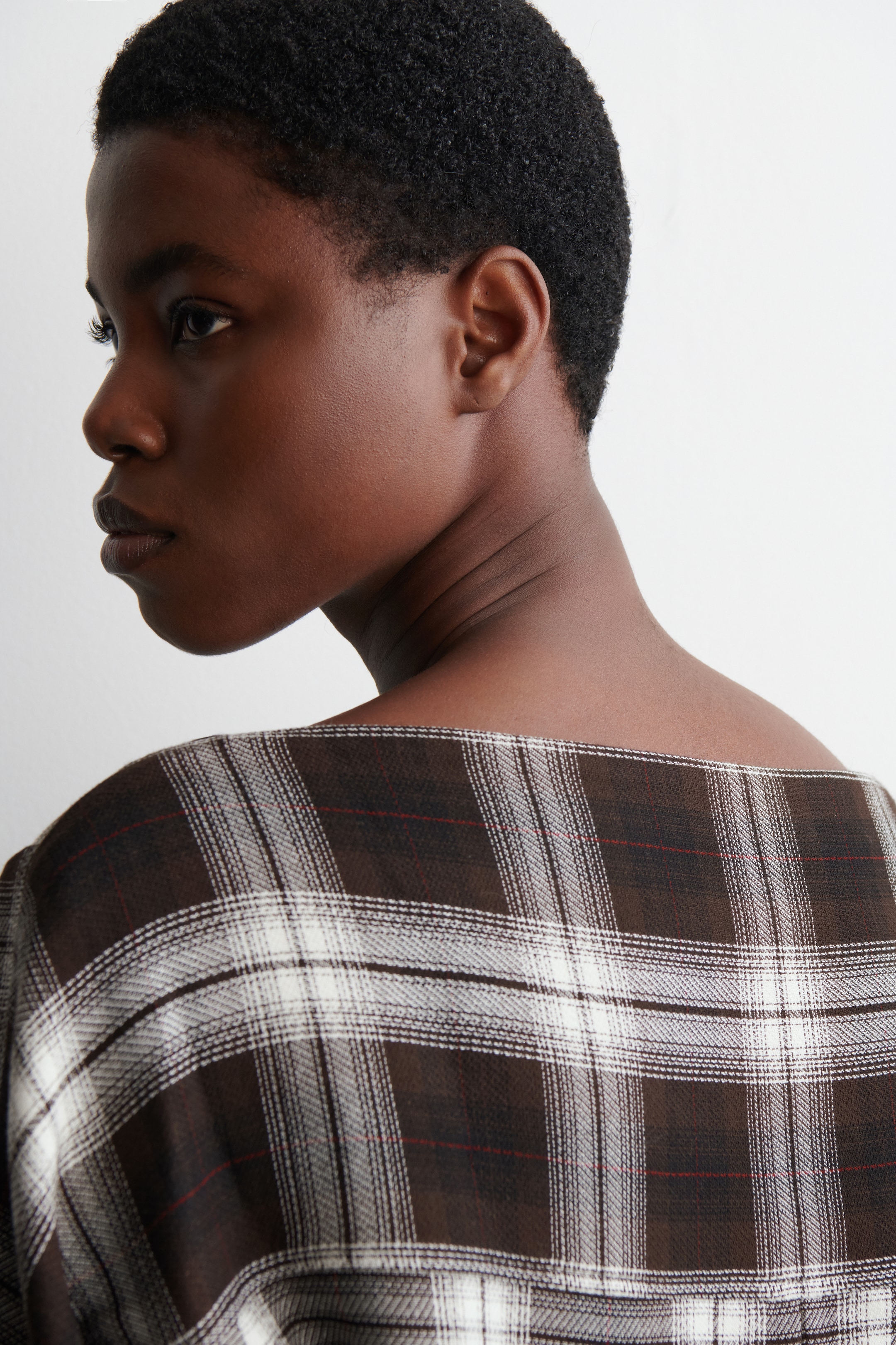 Agrandir l'image: Un haut à carreaux dans les tons de marron, de bordeaux et de blanc cassé est porté par le mannequin. Le haut présente un large décolleté qui s'étend sur le dos et les épaules du mannequin.