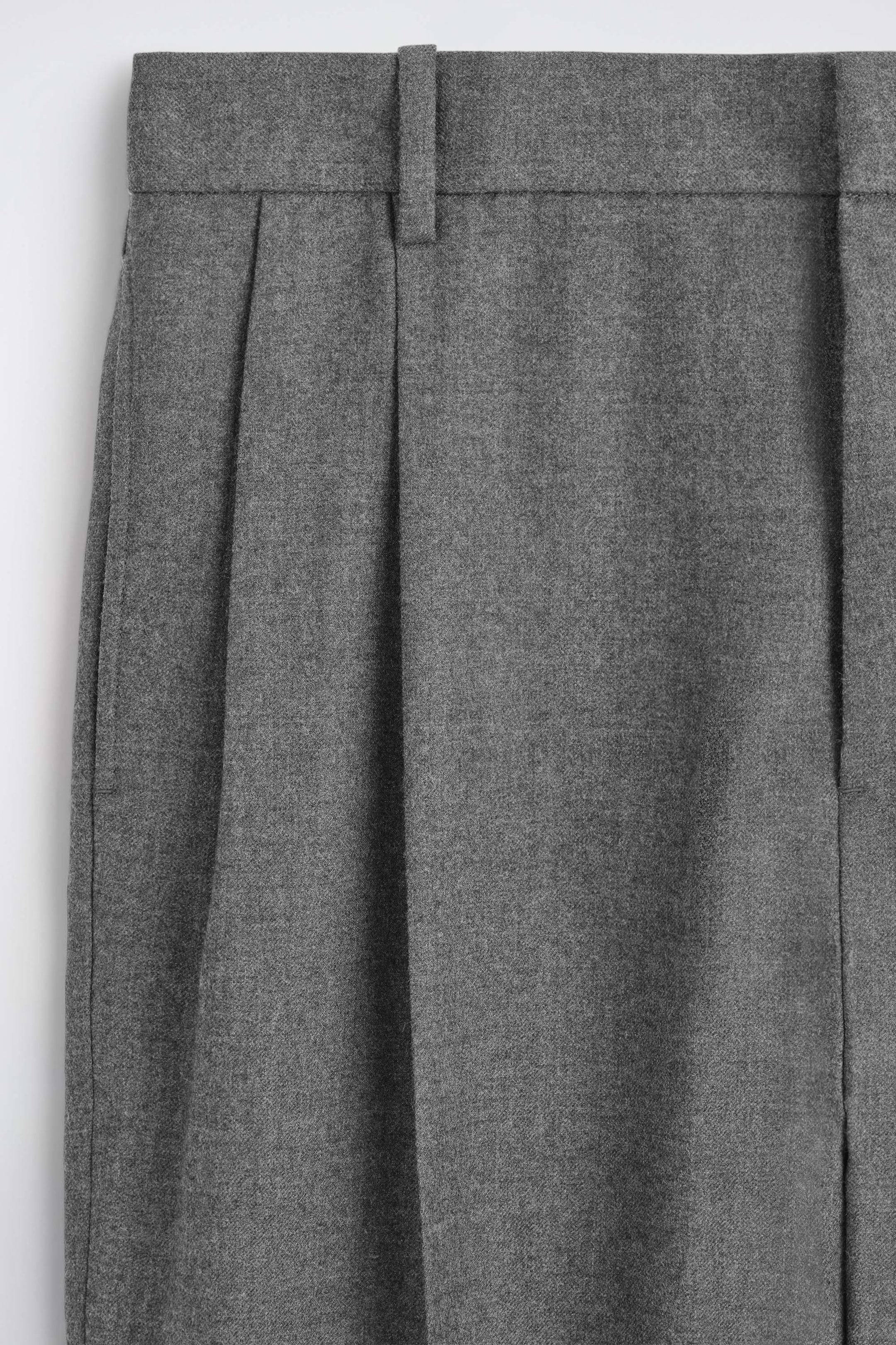 Eine Nahaufnahme einer grauen Hose zeigt einen strukturierten Bund mit einer einzelnen Gürtelschlaufe und markanten Bundfalten vorne. Der melierte Stoff weist eine weiche, gebürstete Textur auf. Eine Nahaufnahme einer grauen Hose zeigt einen strukturierten Bund mit einer einzelnen Gürtelschlaufe und markanten Bundfalten vorne. Der melierte Stoff weist eine weiche, gebürstete Textur auf.