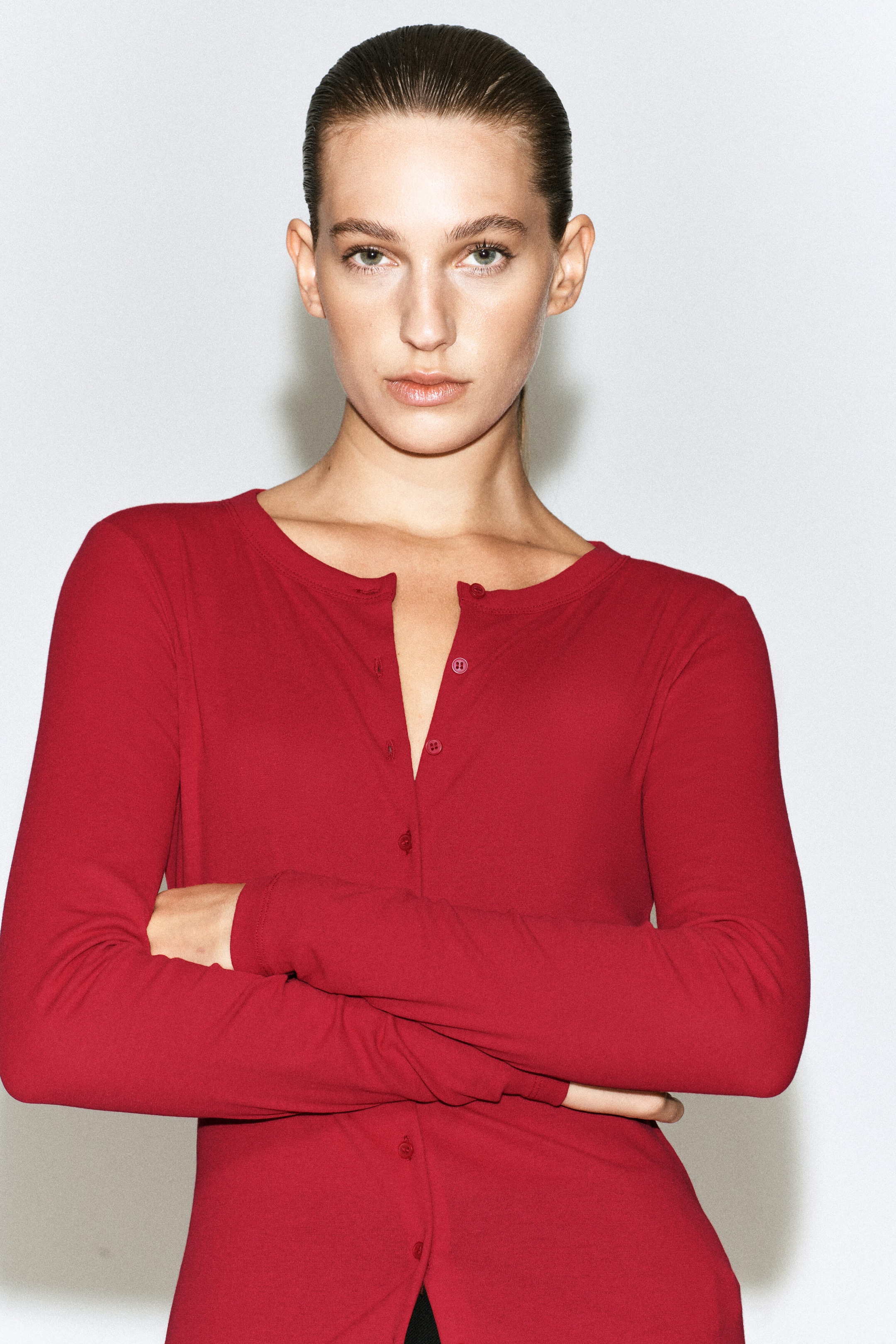 A red jersey cardigan top featuring long sleeves, a round neckline, and a front button closure is being worn by the model. The top is styled with the upper buttons undone, and the model is standing with arms crossed. A red jersey cardigan top featuring long sleeves, a round neckline, and a front button closure is being worn by the model. The top is styled with the upper buttons undone, and the model is standing with arms crossed.