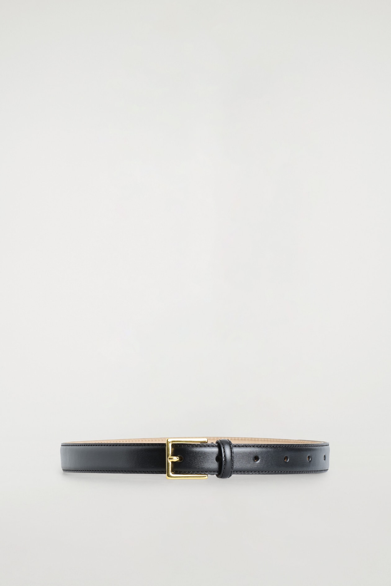 A square-buckle leather belt is arranged in a closed loop facing forward, showcasing a smooth black leather strap with tonal edge stitching and a contrasting light tan interior lining. The belt features a rectangular, gold-tone metal buckle with a single prong and a matching black leather keeper loop next to several pre-punched adjustment holes.