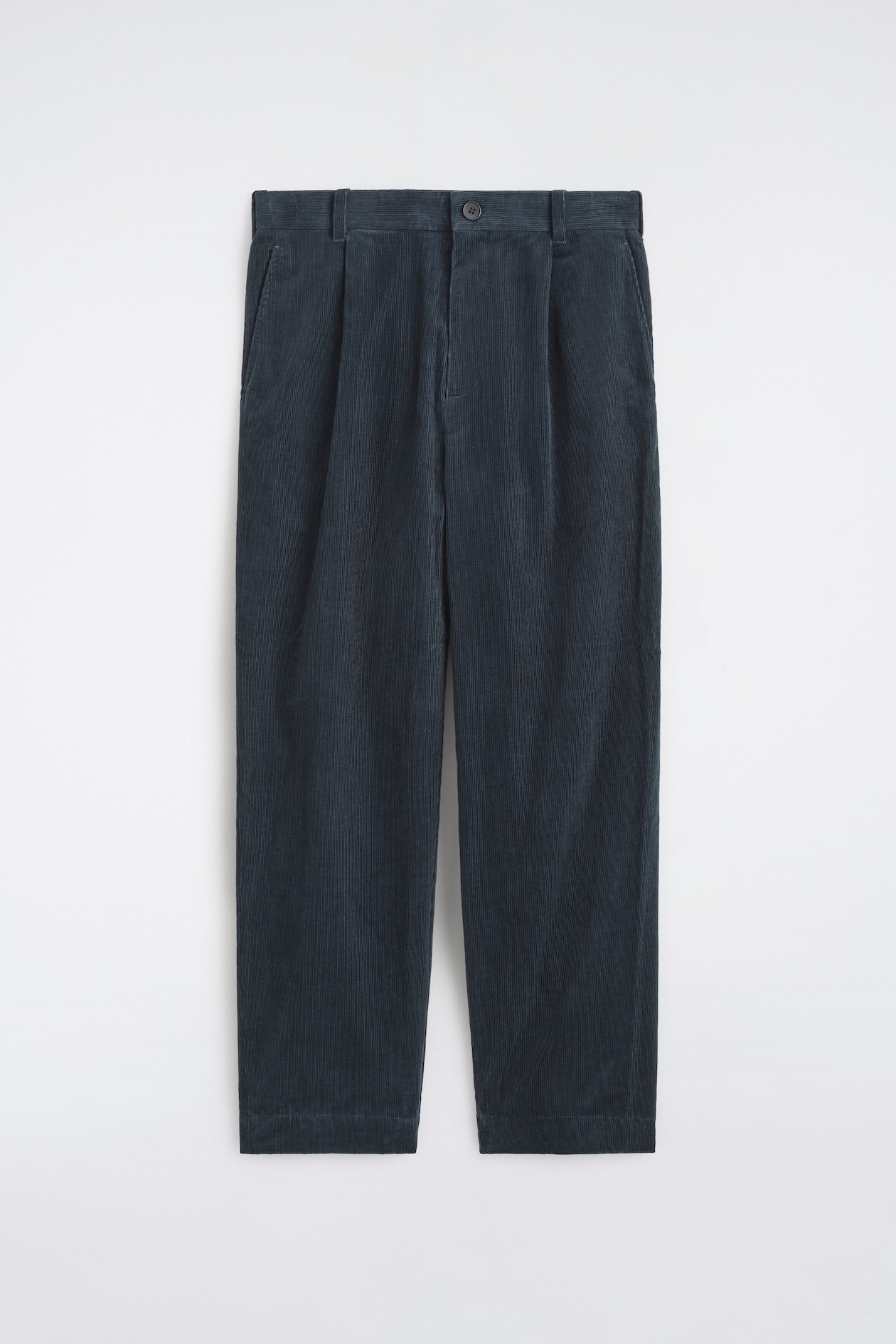 These corduroy relaxed-fit tapered pants are shown in a front view, featuring a dark teal-blue ribbed fabric with front pleats and a button-fastened waistband. The pants display a relaxed silhouette with belt loops, side slit pockets, and legs tapering toward the hem.