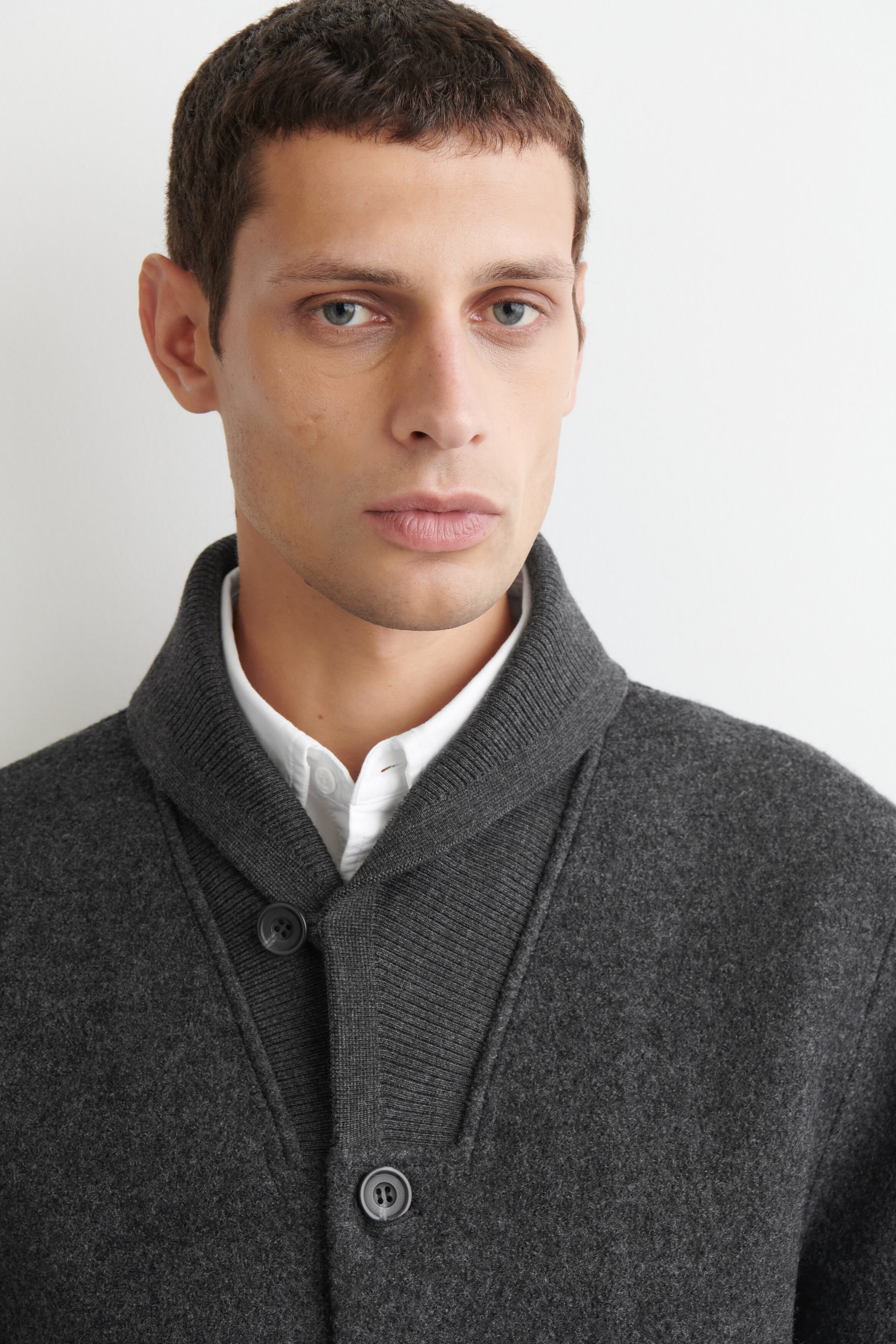 The boiled-wool shawl-collar jacket in charcoal gray is shown in a close-up view, highlighting its ribbed knit shawl collar and button-front closure. The jacket is worn layered over a white button-down shirt, emphasizing the textured finish of the boiled-wool material. The boiled-wool shawl-collar jacket in charcoal gray is shown in a close-up view, highlighting its ribbed knit shawl collar and button-front closure. The jacket is worn layered over a white button-down shirt, emphasizing the textured finish of the boiled-wool material.