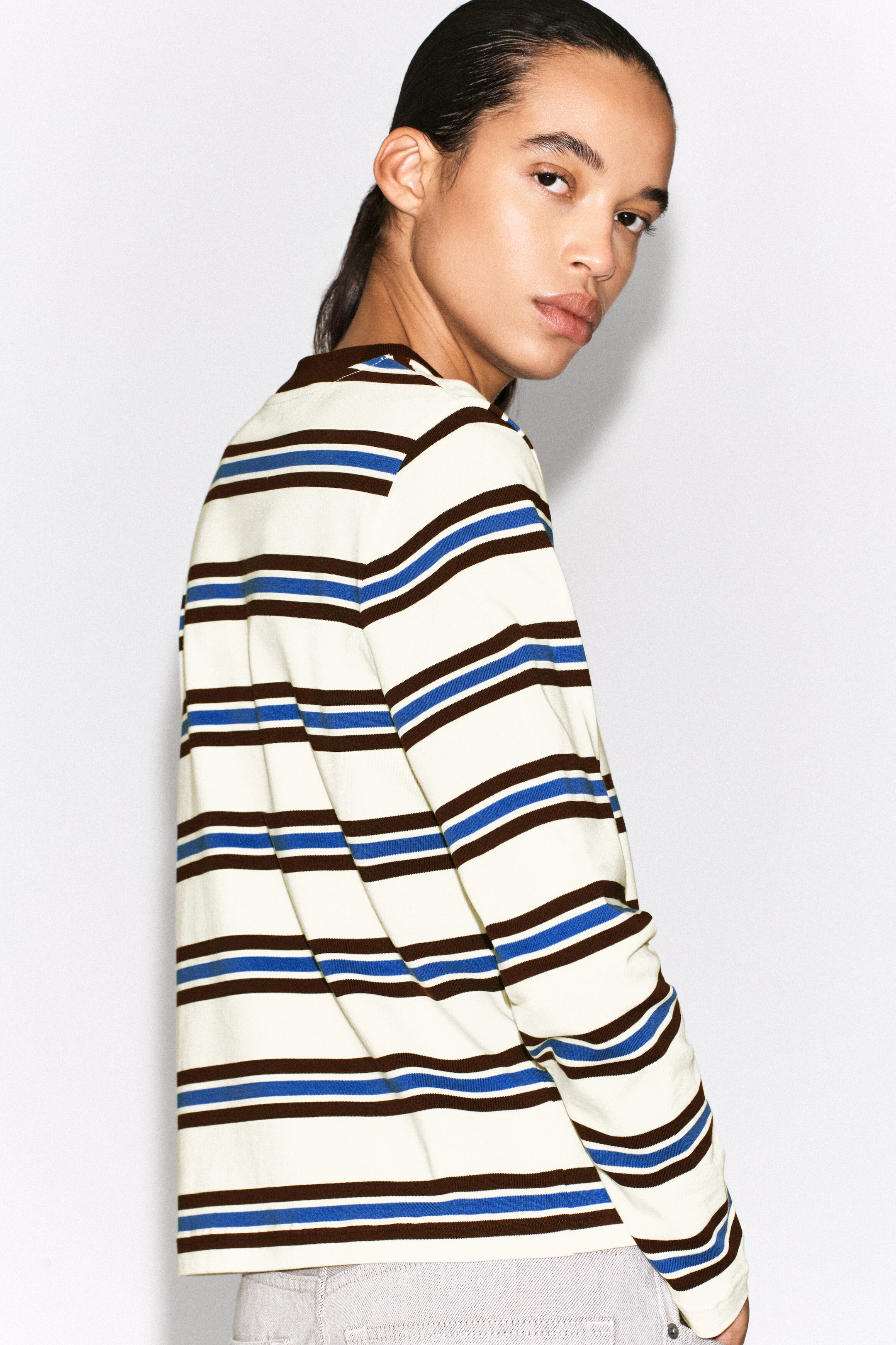 The clean-cut long-sleeved T-shirt is shown from a back-angled view, displaying a pattern of horizontal cream, brown, and blue stripes. It features long sleeves and a brown crew neckline. The clean-cut long-sleeved T-shirt is shown from a back-angled view, displaying a pattern of horizontal cream, brown, and blue stripes. It features long sleeves and a brown crew neckline.