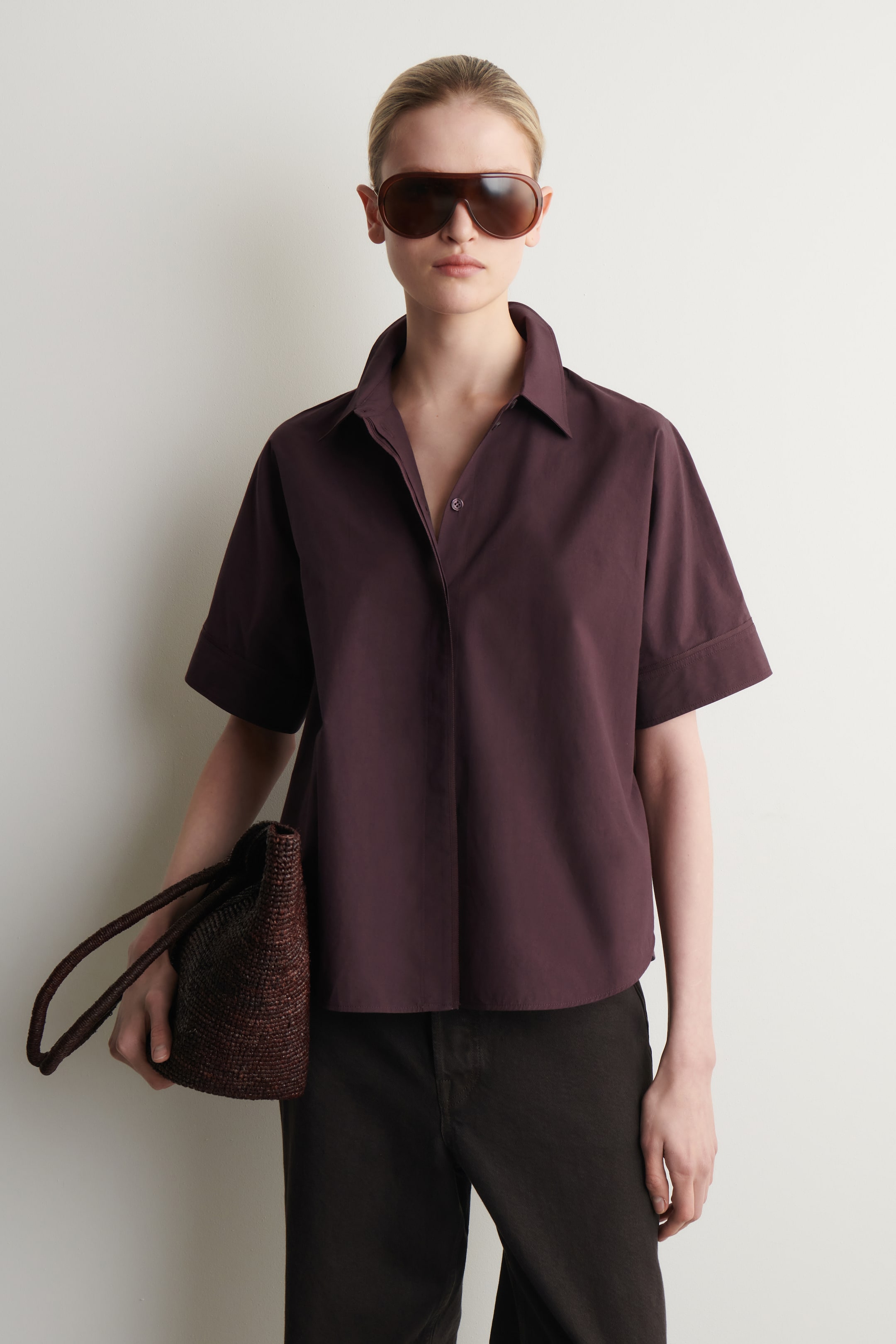 Agrandir l'image: Une chemise à manches courtes prune foncé est dotée d'un col pointu et de larges manches retroussées. La chemise est conçue avec une coupe décontractée, et sa patte de boutonnage avant est partiellement déboutonnée, créant une ouverture en V.