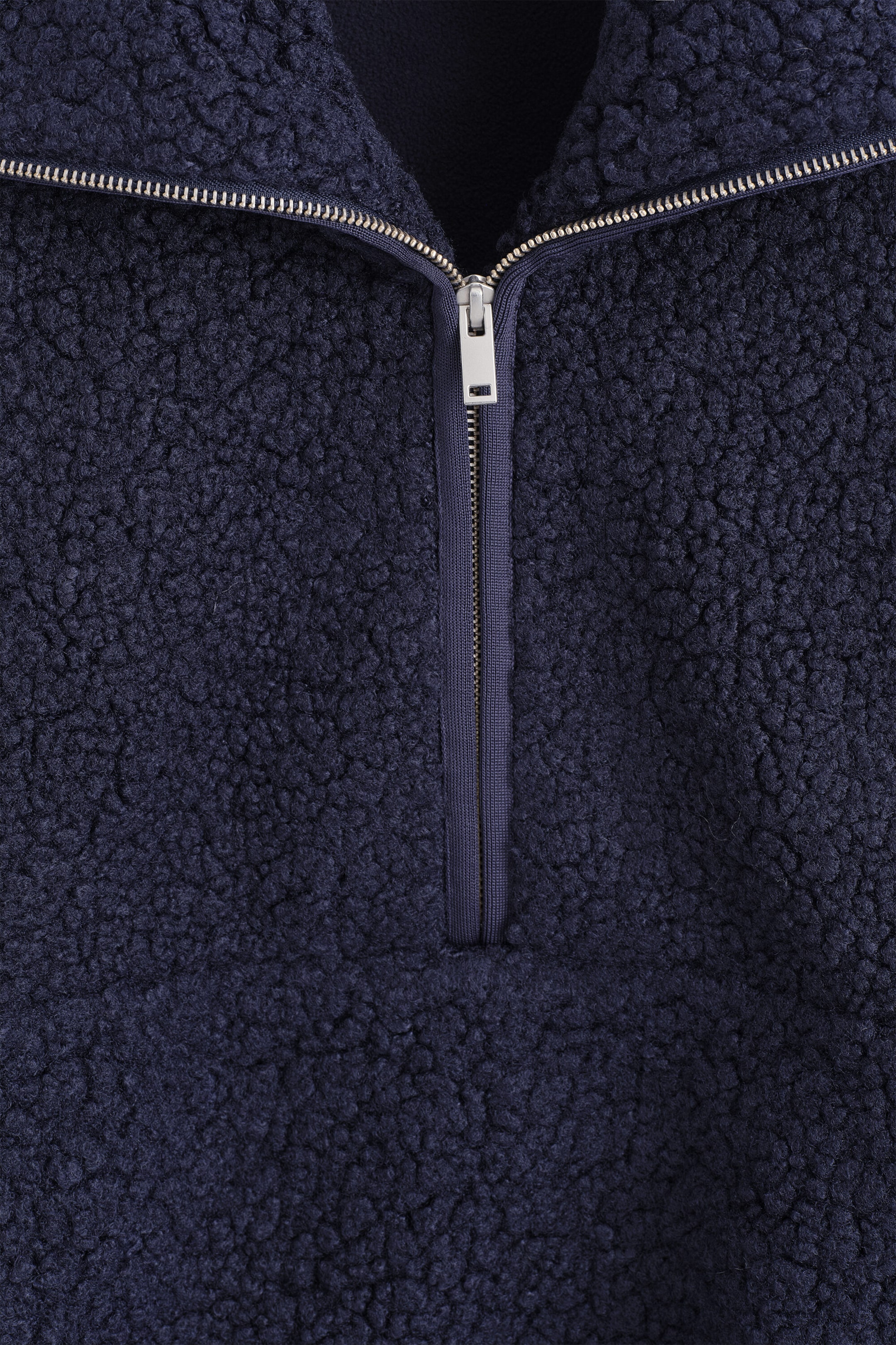 A close-up view showcases a navy blue funnel-neck teddy zip-up jumper featuring textured, curly fleece fabric. A silver-toned metal half-zipper runs down the center front, remaining partially open to show the collar construction. A close-up view showcases a navy blue funnel-neck teddy zip-up jumper featuring textured, curly fleece fabric. A silver-toned metal half-zipper runs down the center front, remaining partially open to show the collar construction.