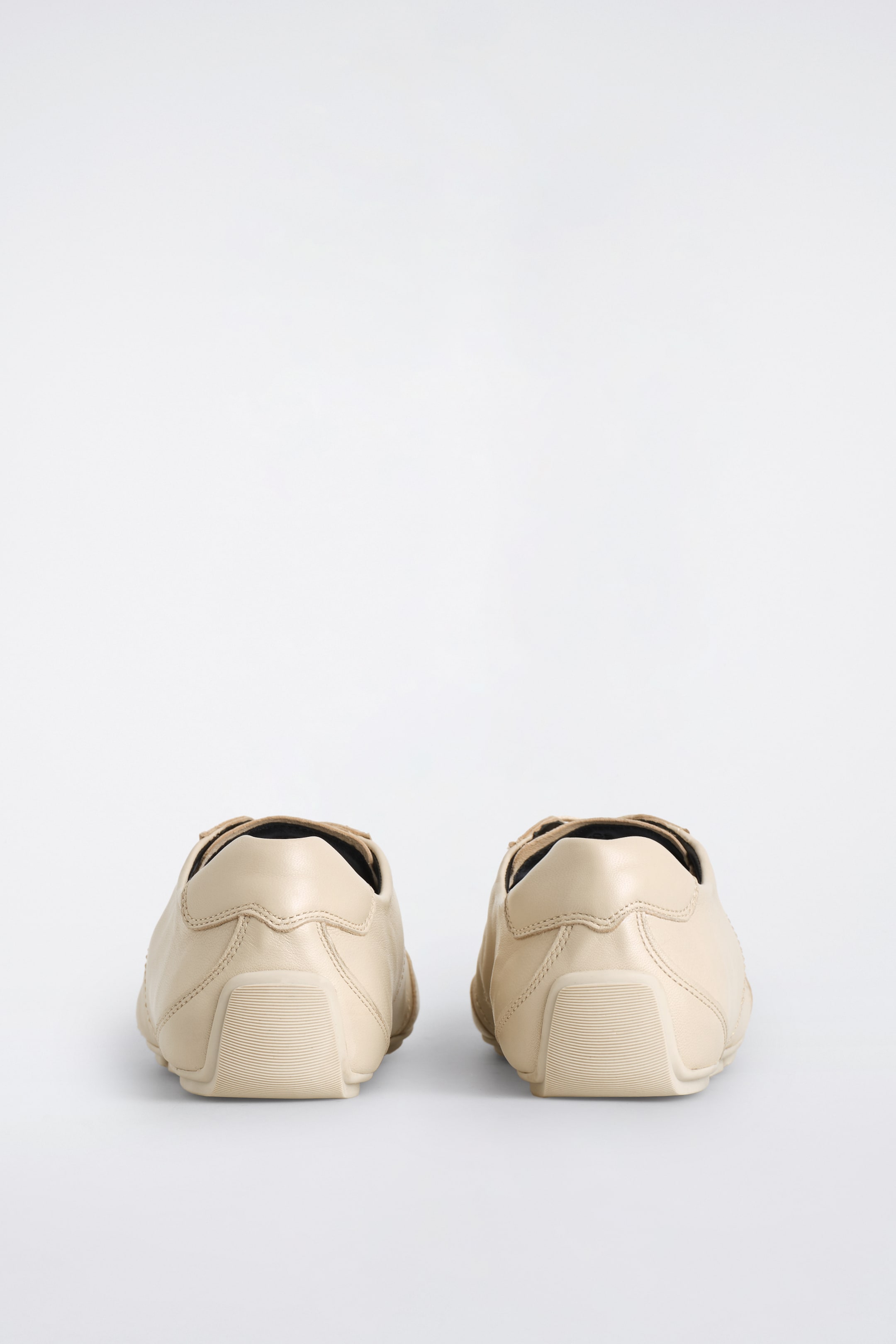 Größeres Bild ansehen: Zwei hellbeige Leder-Sneaker sind von hinten zu sehen und zeigen schlanke Silhouetten. Sie verfügen über tonale Steppnähte an den Fersenkappen und ruhen auf gerippten Gummisohlen.