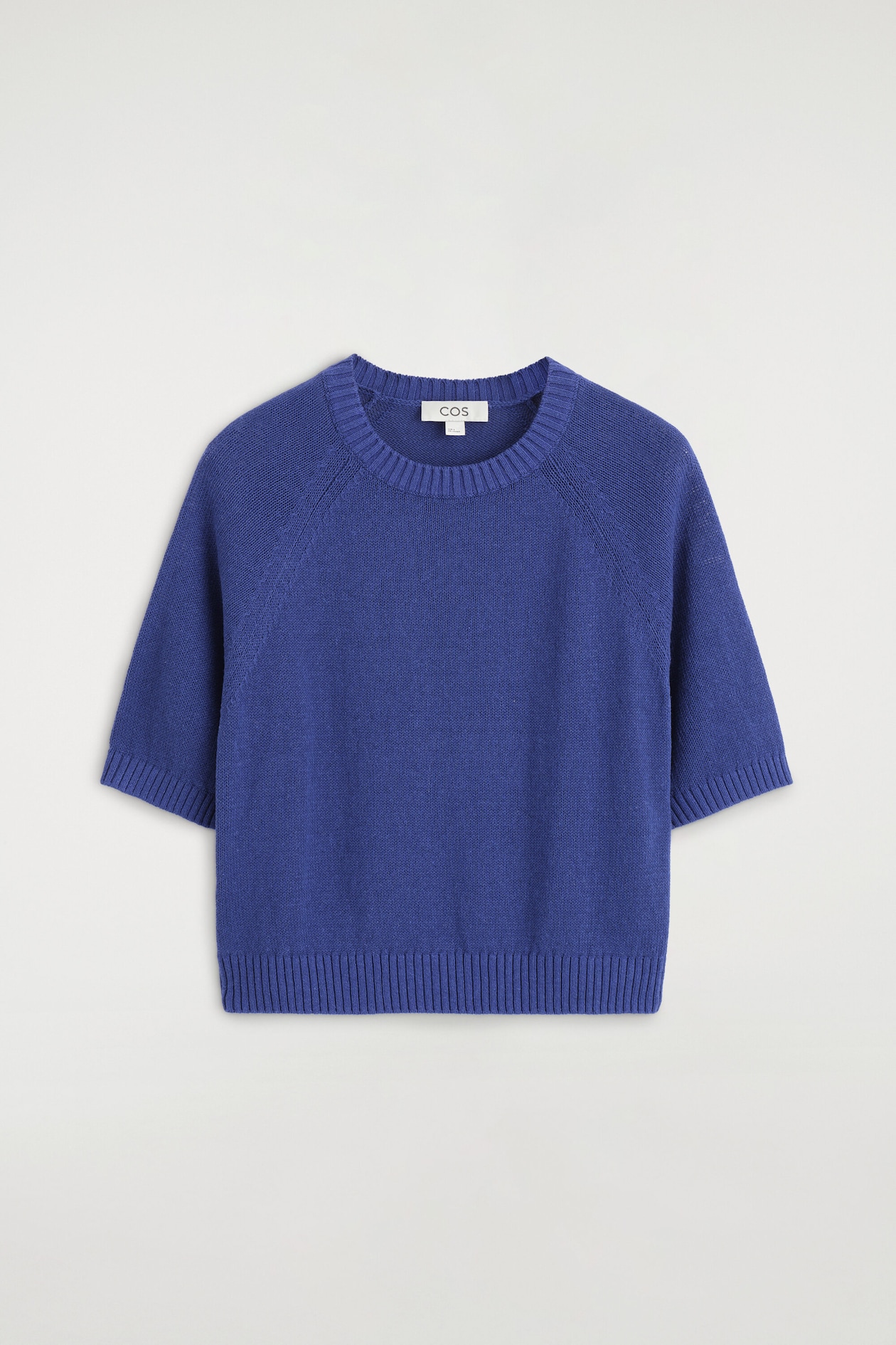 The shrunken knitted linen T-shirt is facing front, featuring a vibrant blue knit design with a ribbed crew neck, raglan short sleeves, and a ribbed hem and cuffs.