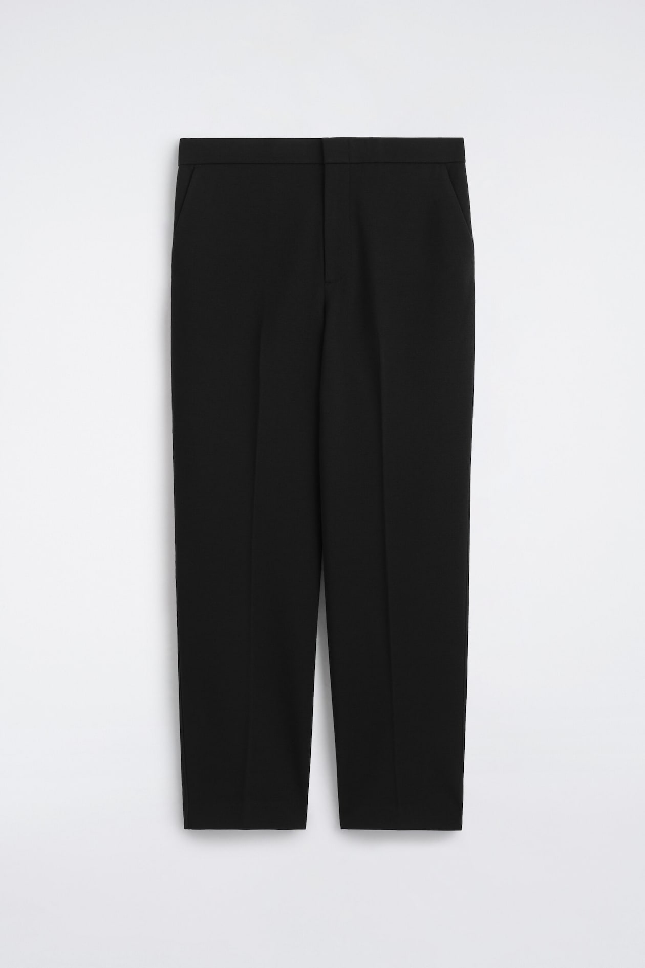 These black tailored trousers are shown from the front, featuring a straight-leg silhouette with sharp pressed creases running down the center of each leg. The design showcases a clean, minimalist waistband with subtle side slit pockets and a concealed front fastening.