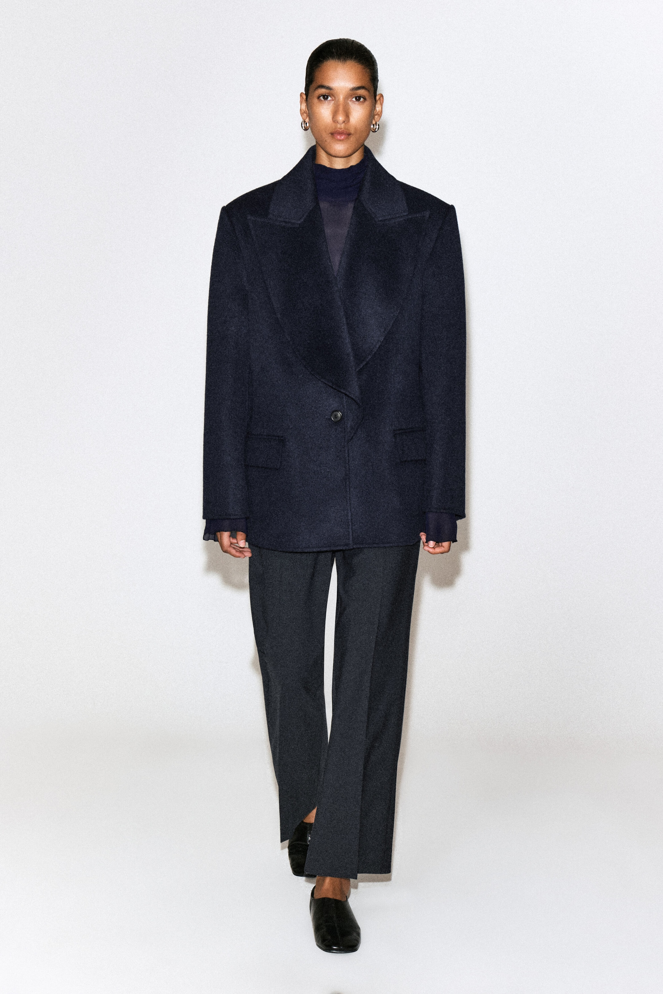 The dark grey twill cropped flared pants feature a structured, straight-leg fit with a subtle flare and a sharp pressed crease running down each leg. Shown from the front, the pants display a cropped length with small slits at the front hem.