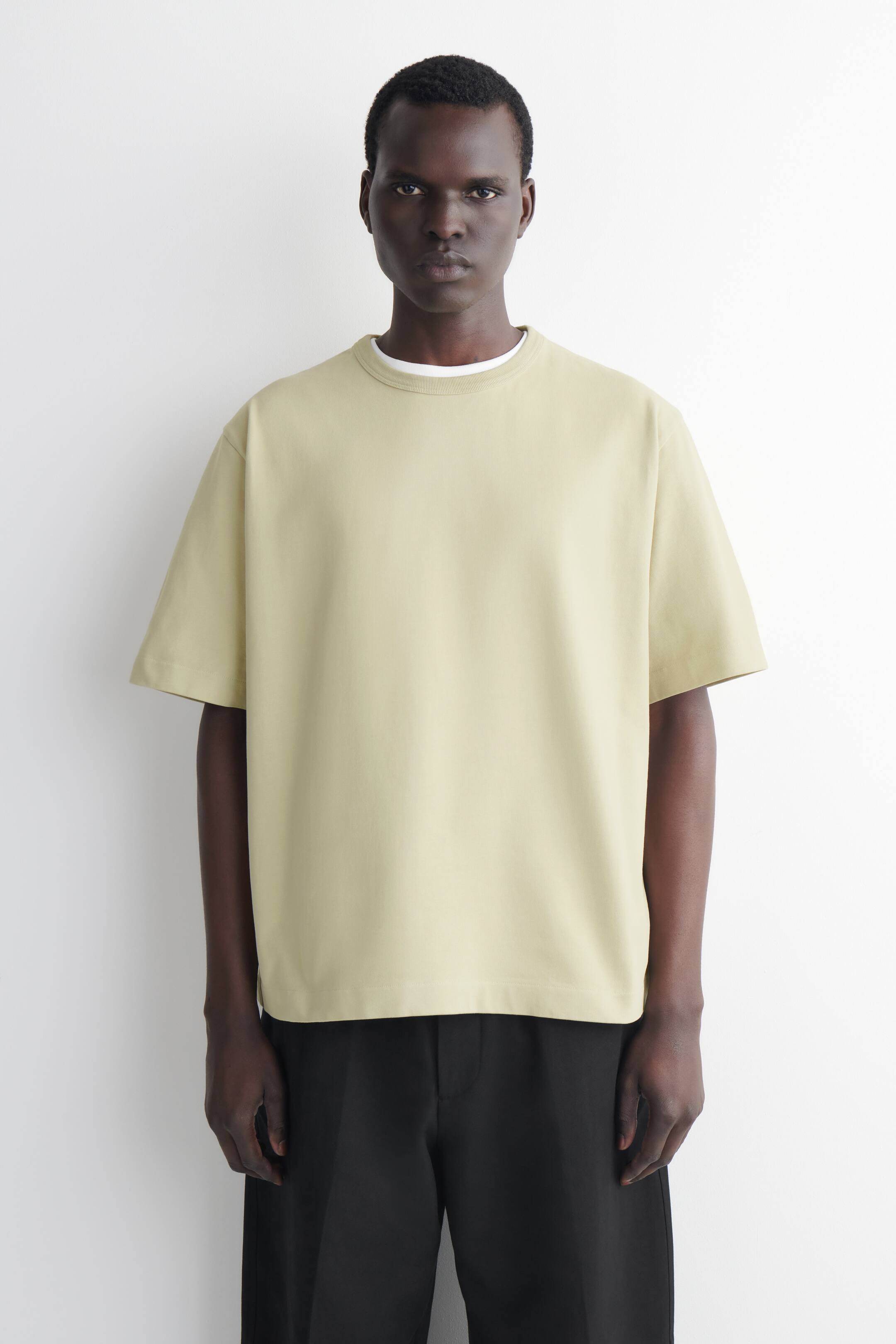 View larger image: A pale yellow-green T-shirt is being worn, facing forward, featuring a relaxed fit, short sleeves, and a crew neck, with a white crew neck shirt visible underneath its neckline.