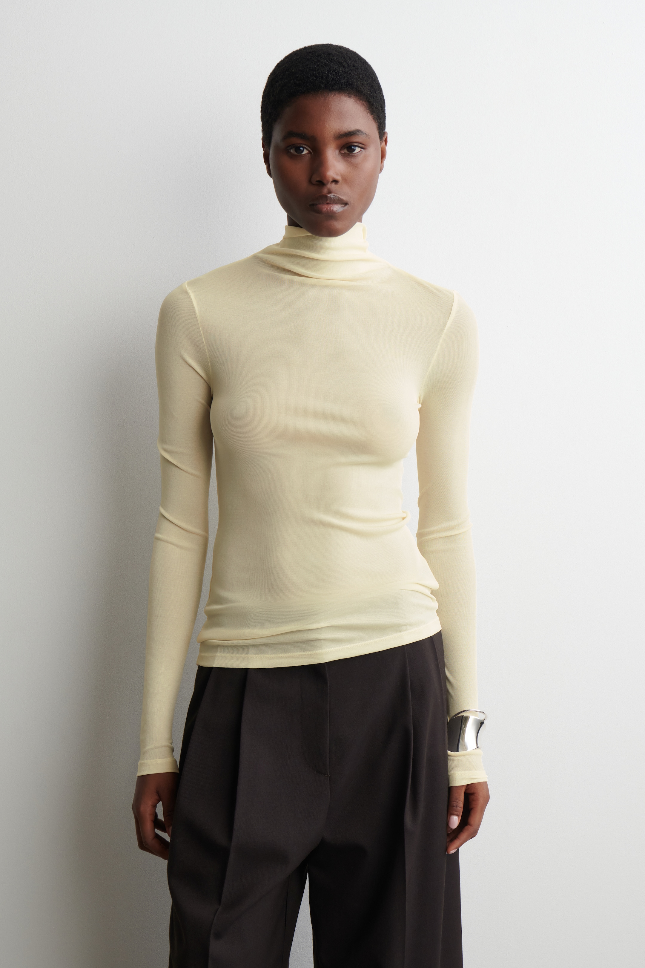 Agrandir l'image: Un haut à col roulé jaune pâle est présenté, avec un tissu léger et transparent et une silhouette ajustée avec des manches longues. Le col roulé haut est délicatement froncé autour du cou.