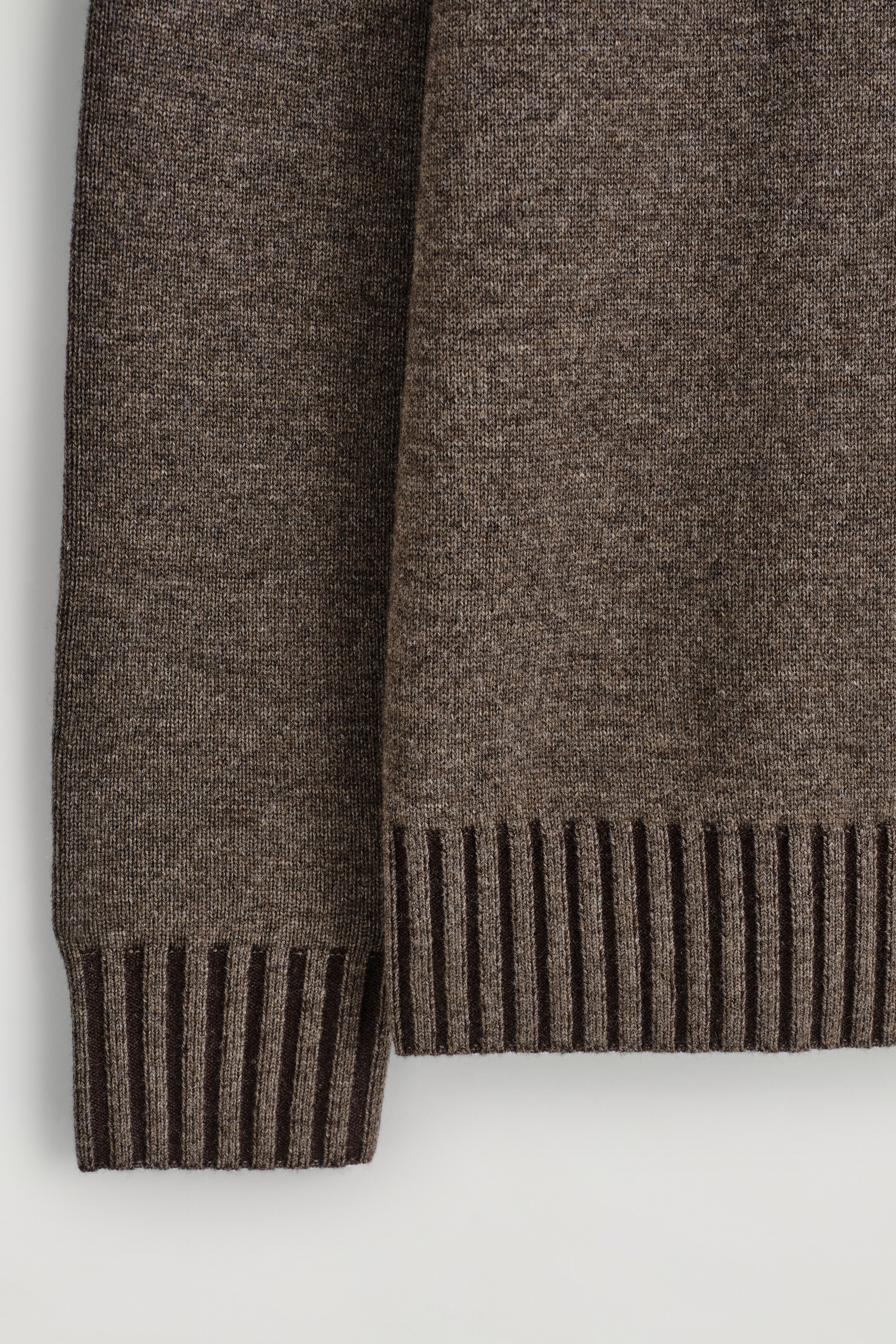 View larger image: A brown heathered knitted garment is prominently displaying its fine knit texture, with a darker brown ribbed cuff visible on the left and a matching ribbed hem on the right, both featuring distinct vertical ribbing.