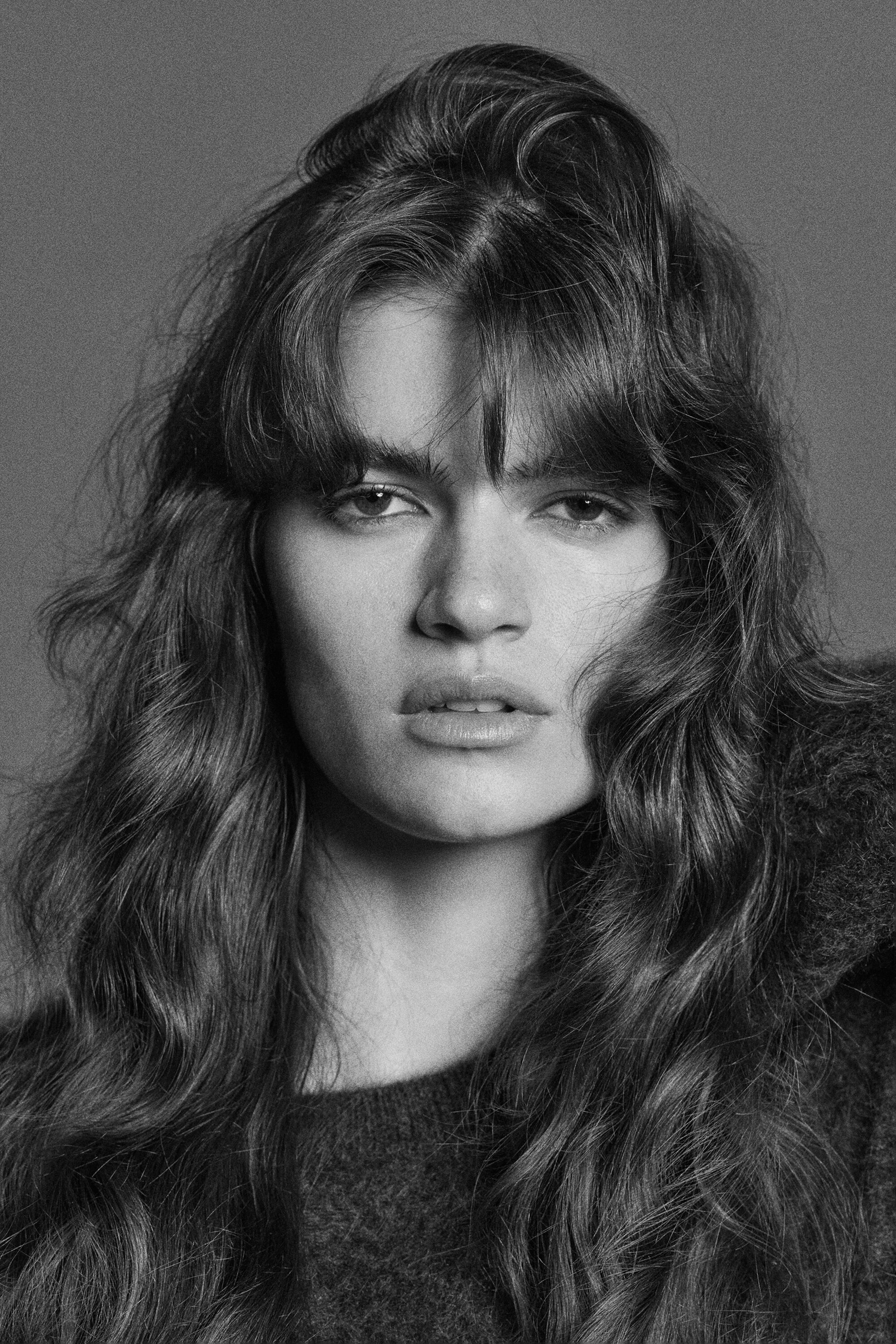 A dark-toned crew-neck sweater is being worn in a front-facing close-up, showcasing its soft, brushed knit texture around the neckline. A dark-toned crew-neck sweater is being worn in a front-facing close-up, showcasing its soft, brushed knit texture around the neckline.