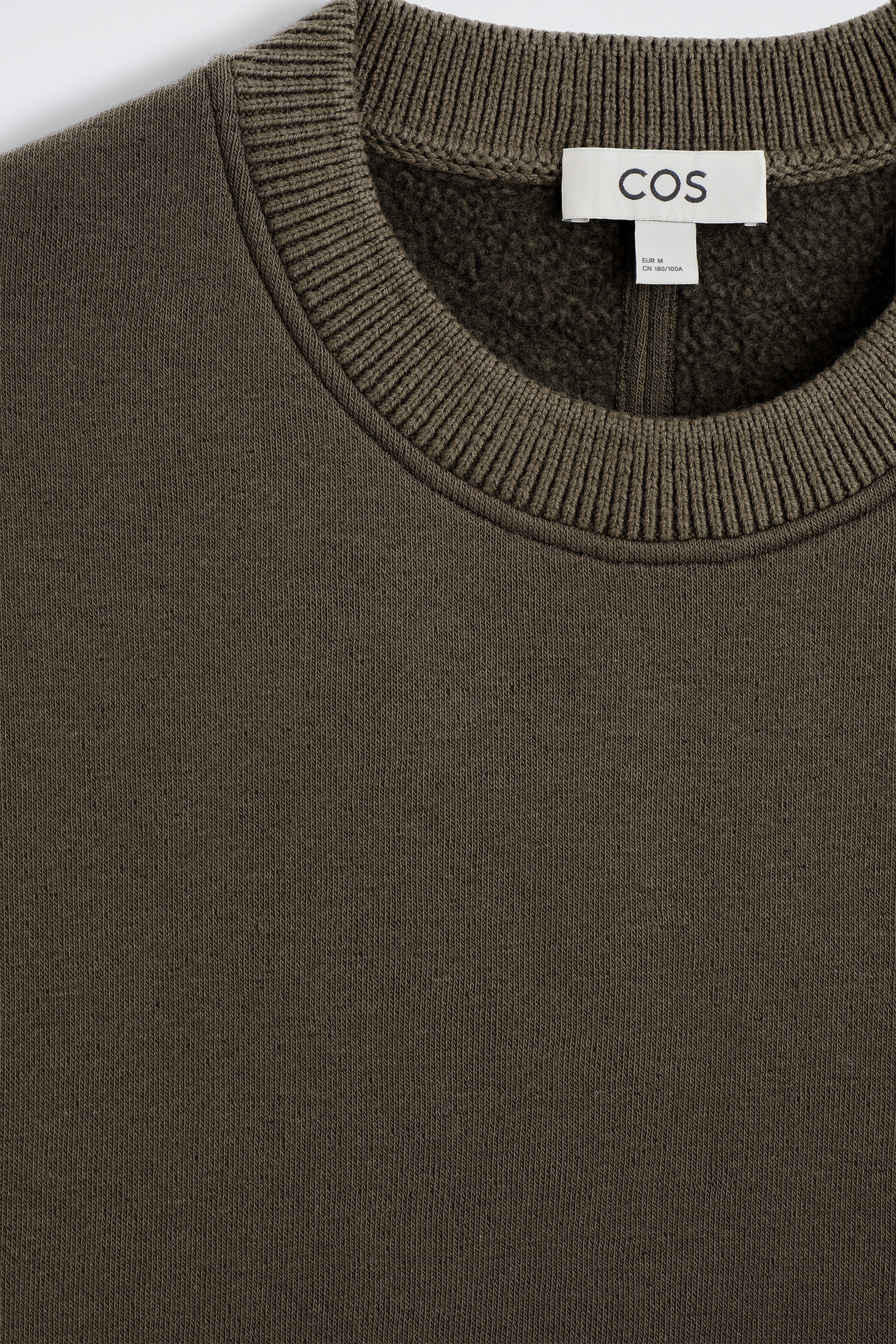Un chandail en jersey de coton et de laine présente, en gros plan de face, une texture fine tricotée de couleur vert olive foncé et un col rond épais côtelé. L’intérieur révèle une doublure en molleton douce et duveteuse, avec une étiquette de marque blanche cousue au centre du dos. Un chandail en jersey de coton et de laine présente, en gros plan de face, une texture fine tricotée de couleur vert olive foncé et un col rond épais côtelé. L’intérieur révèle une doublure en molleton douce et duveteuse, avec une étiquette de marque blanche cousue au centre du dos.