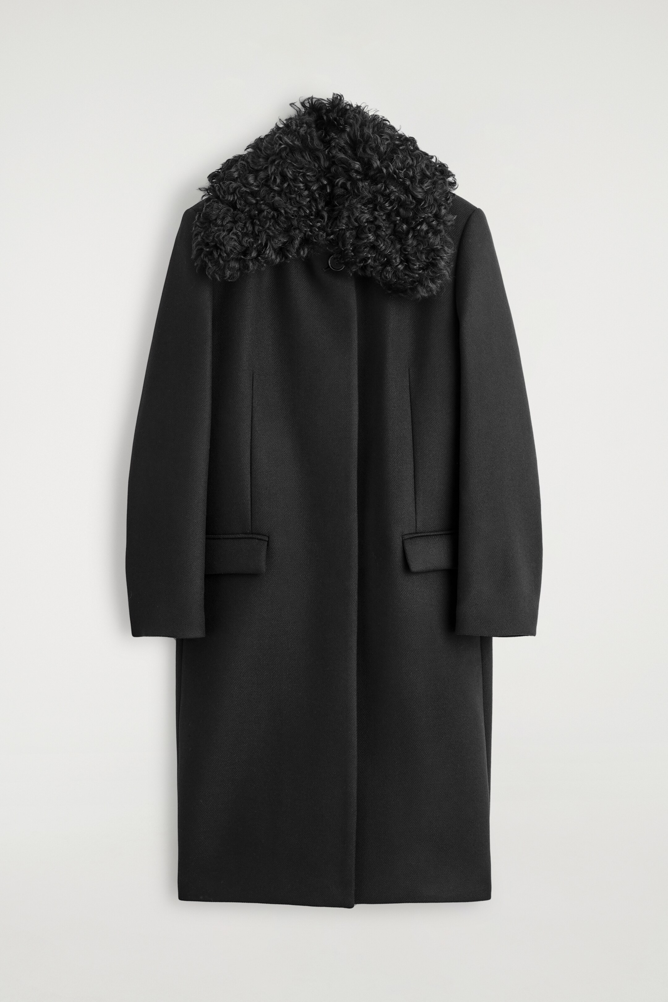 View larger image: A black long coat is presenting its front, featuring a curly textured black collar, a concealed button placket, and two rectangular flap pockets.