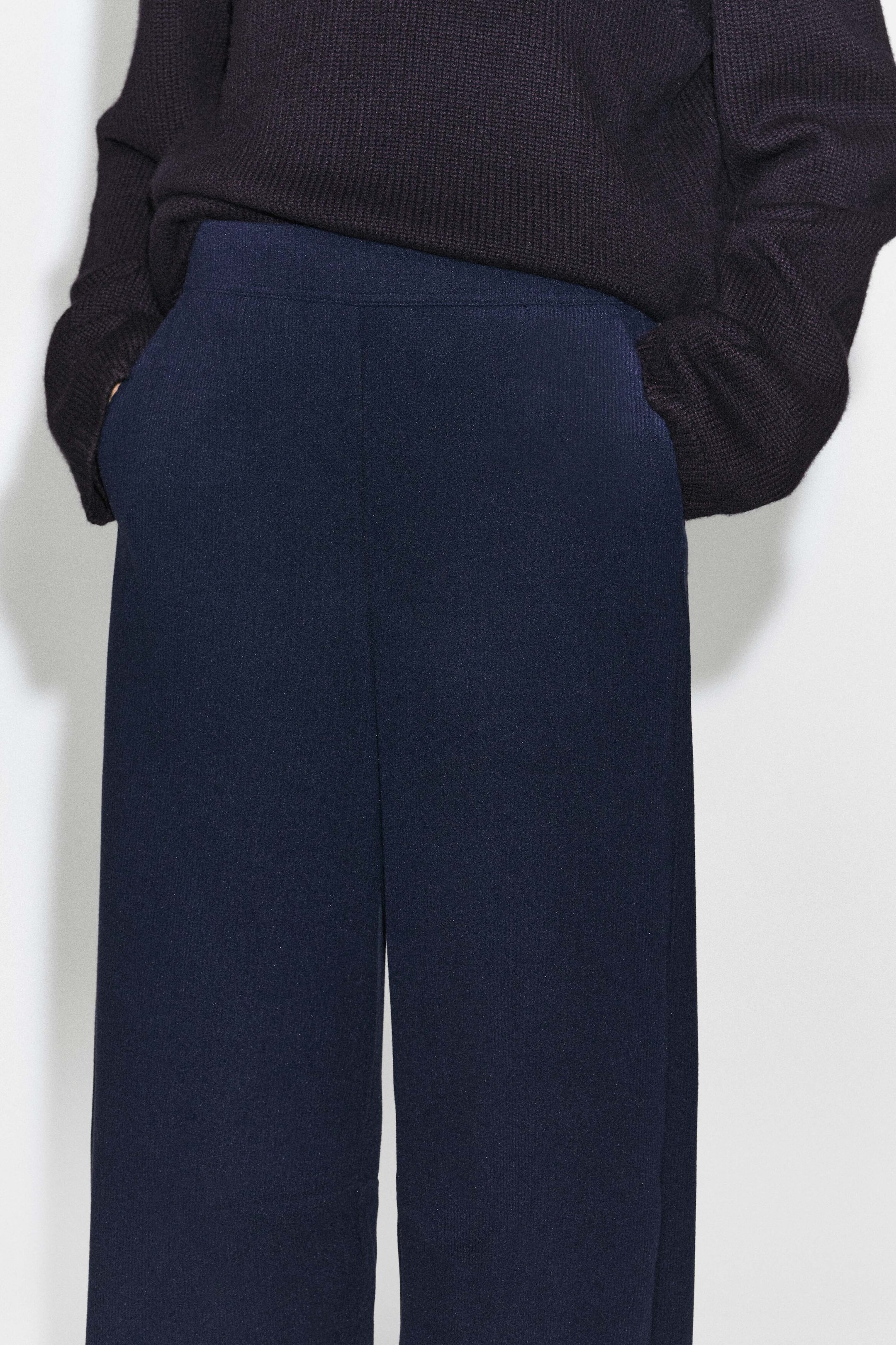 Le mannequin porte un pantalon large en jersey de velours côtelé bleu marine foncé, avec les mains glissées dans les poches latérales. Le pantalon présente une fine texture côtelée et est agencé avec un chandail en tricot texturé foncé porté par-dessus la taille. Le mannequin porte un pantalon large en jersey de velours côtelé bleu marine foncé, avec les mains glissées dans les poches latérales. Le pantalon présente une fine texture côtelée et est agencé avec un chandail en tricot texturé foncé porté par-dessus la taille.