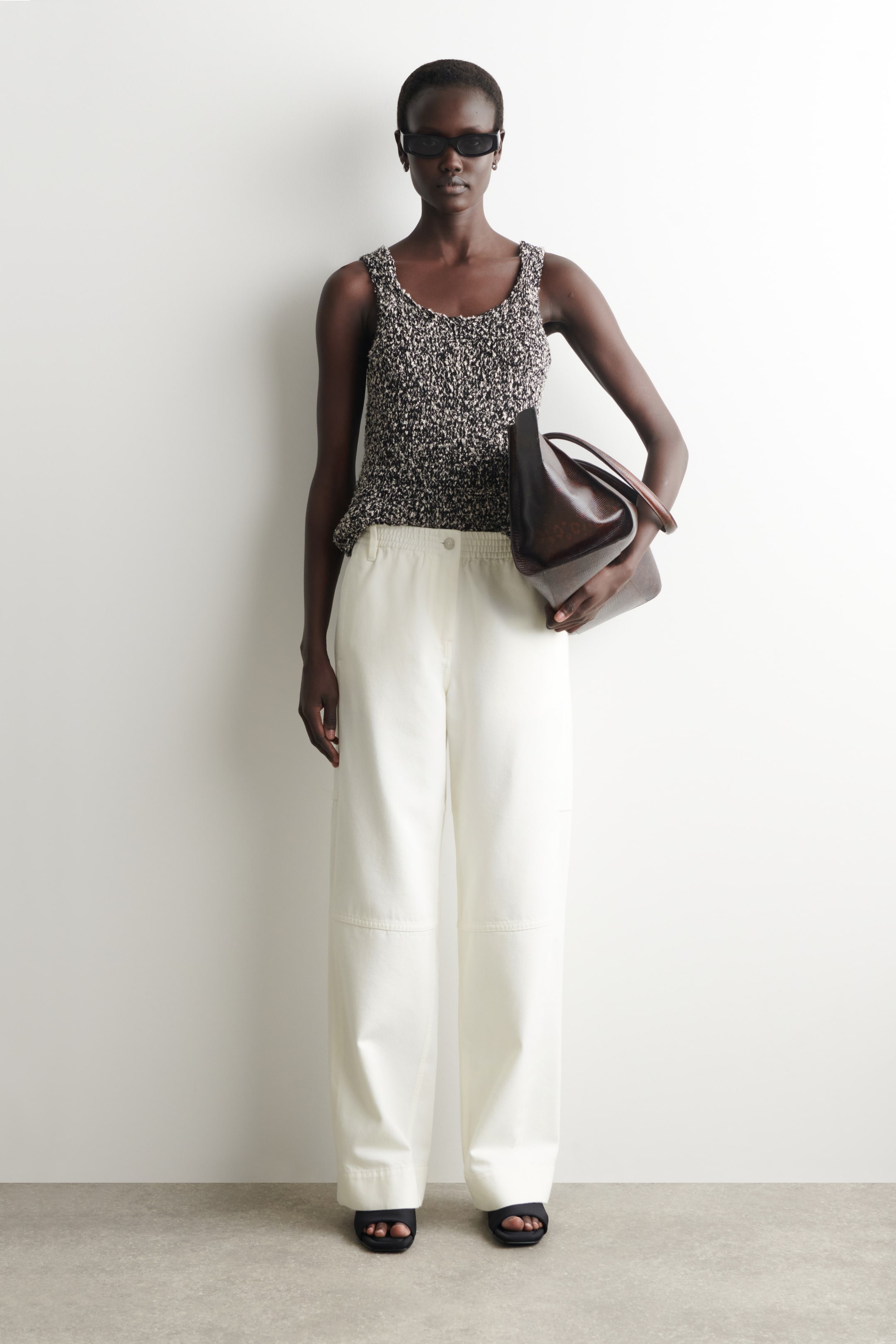 Grotere afbeelding bekijken: De crèmekleurige broek met wijde pijpen heeft een elastische tailleband met een enkele knoopsluiting en horizontale naaddetails bij de knieën. Ze hebben een losse pasvorm, vallen recht naar beneden terwijl ze naar voren gericht zijn.