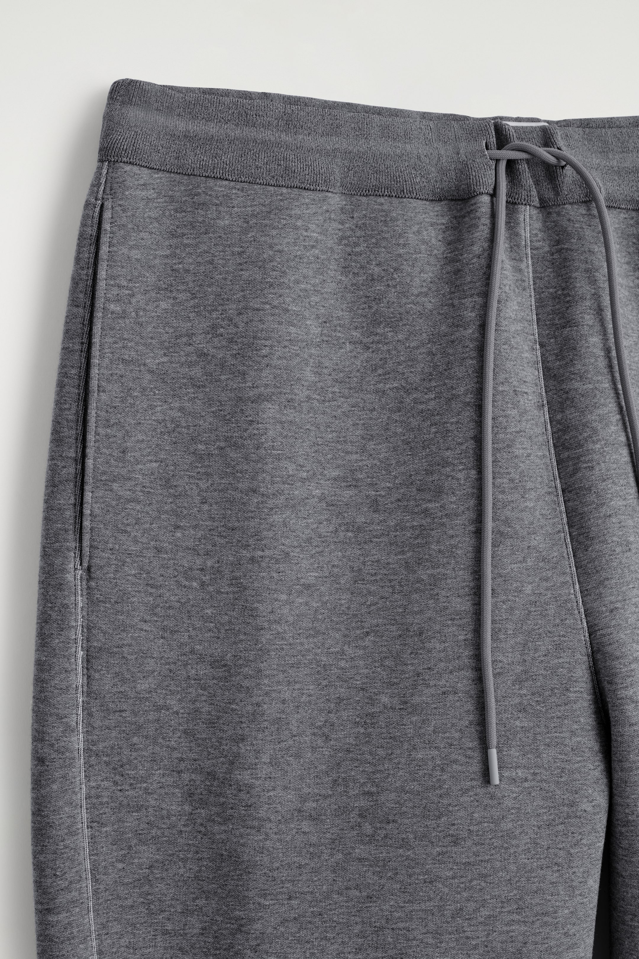 Größeres Bild ansehen: Dunkelgraue Jogginghosen zeigen einen gerippten Bund mit einem verstellbaren Kordelzug. Vertikale Seitentaschen sind auf der Vorderseite des weichen Strickstoffs sichtbar.