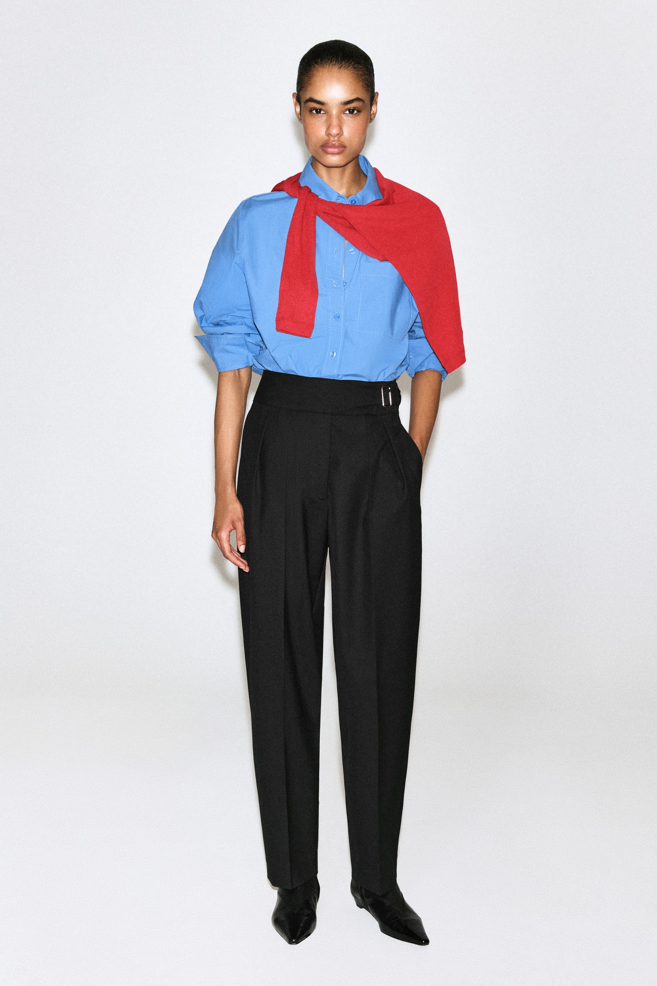 Ver imagen más grande: Estos pantalones negros de pernera barrel se muestran de frente, con una cintura tipo cummerbund de tiro alto con hebilla lateral, pinzas delanteras y marcas de planchado en las perneras. Se combinan con una camisa azul por dentro para destacar el detalle de la cintura y la estructura.