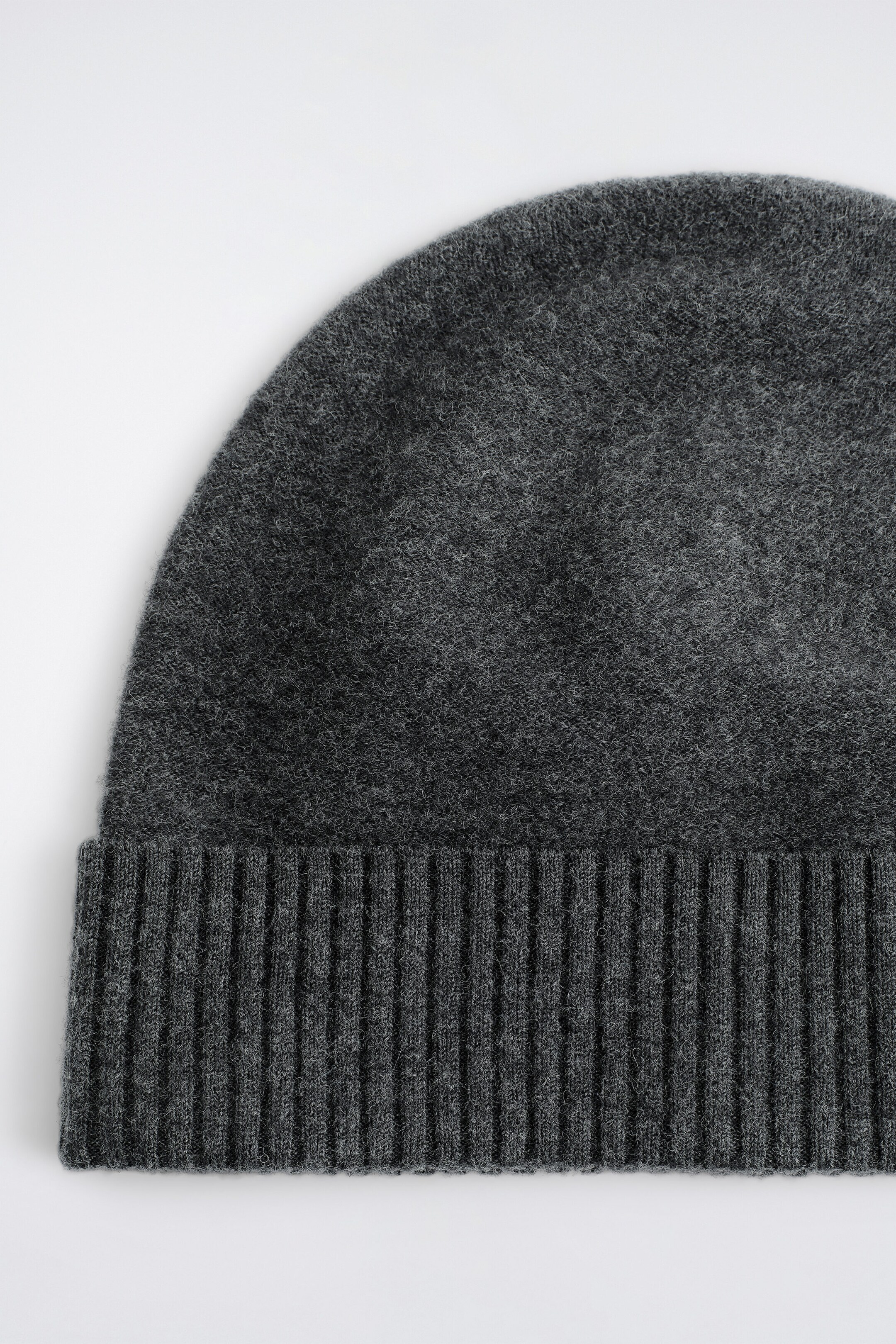 A dark grey boiled wool toque is shown from the front, highlighting its densely knit, textured body and a wide, vertically ribbed fold-up brim.