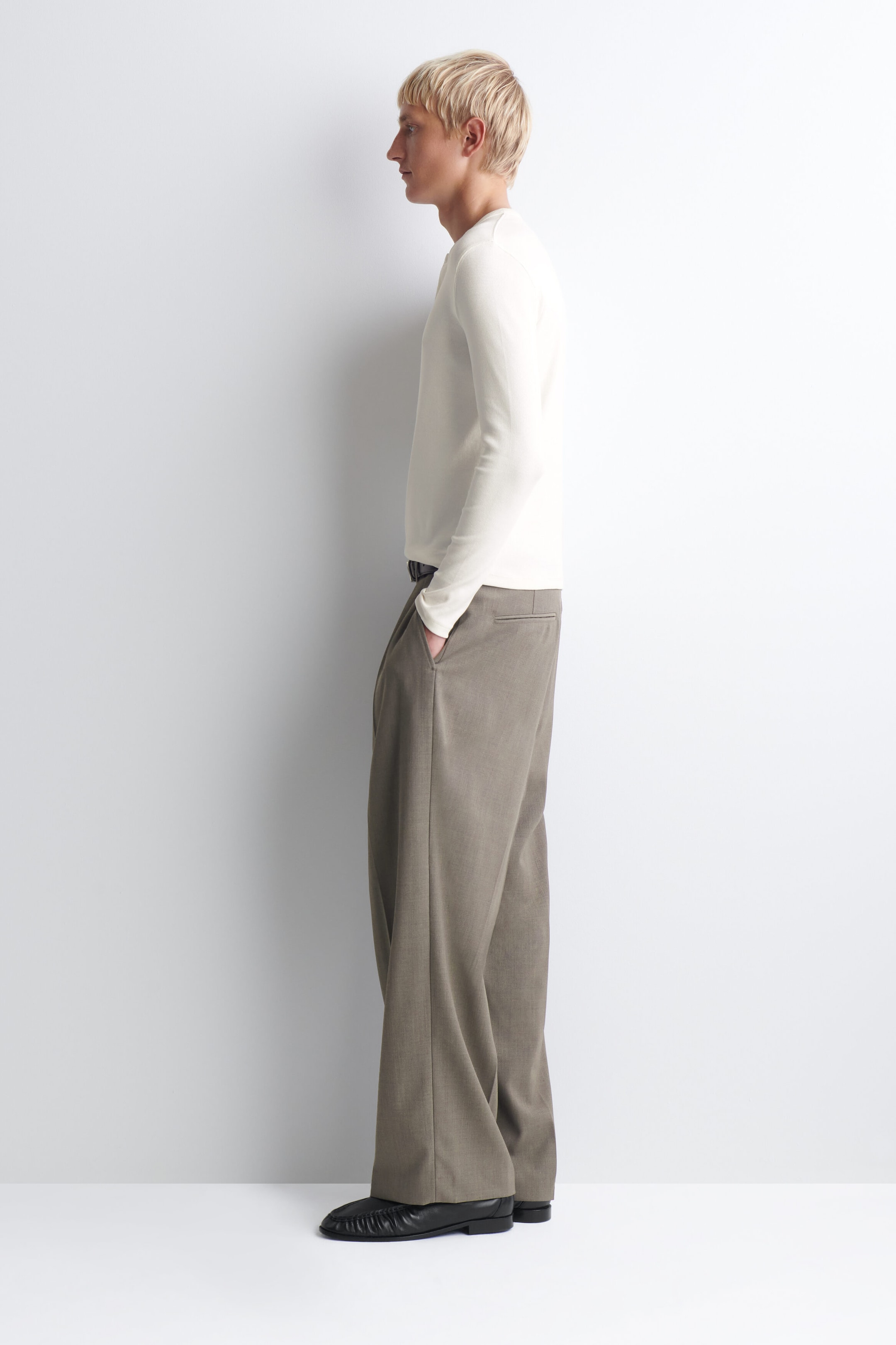 The slim ribbed cotton long-sleeved henley T-shirt in off-white is shown in side profile facing right, highlighting its close-fitting silhouette and fine ribbed texture. The long-sleeved top drapes over the waistband of wide-leg taupe trousers to showcase its casual yet structured fit. The slim ribbed cotton long-sleeved henley T-shirt in off-white is shown in side profile facing right, highlighting its close-fitting silhouette and fine ribbed texture. The long-sleeved top drapes over the waistband of wide-leg taupe trousers to showcase its casual yet structured fit.
