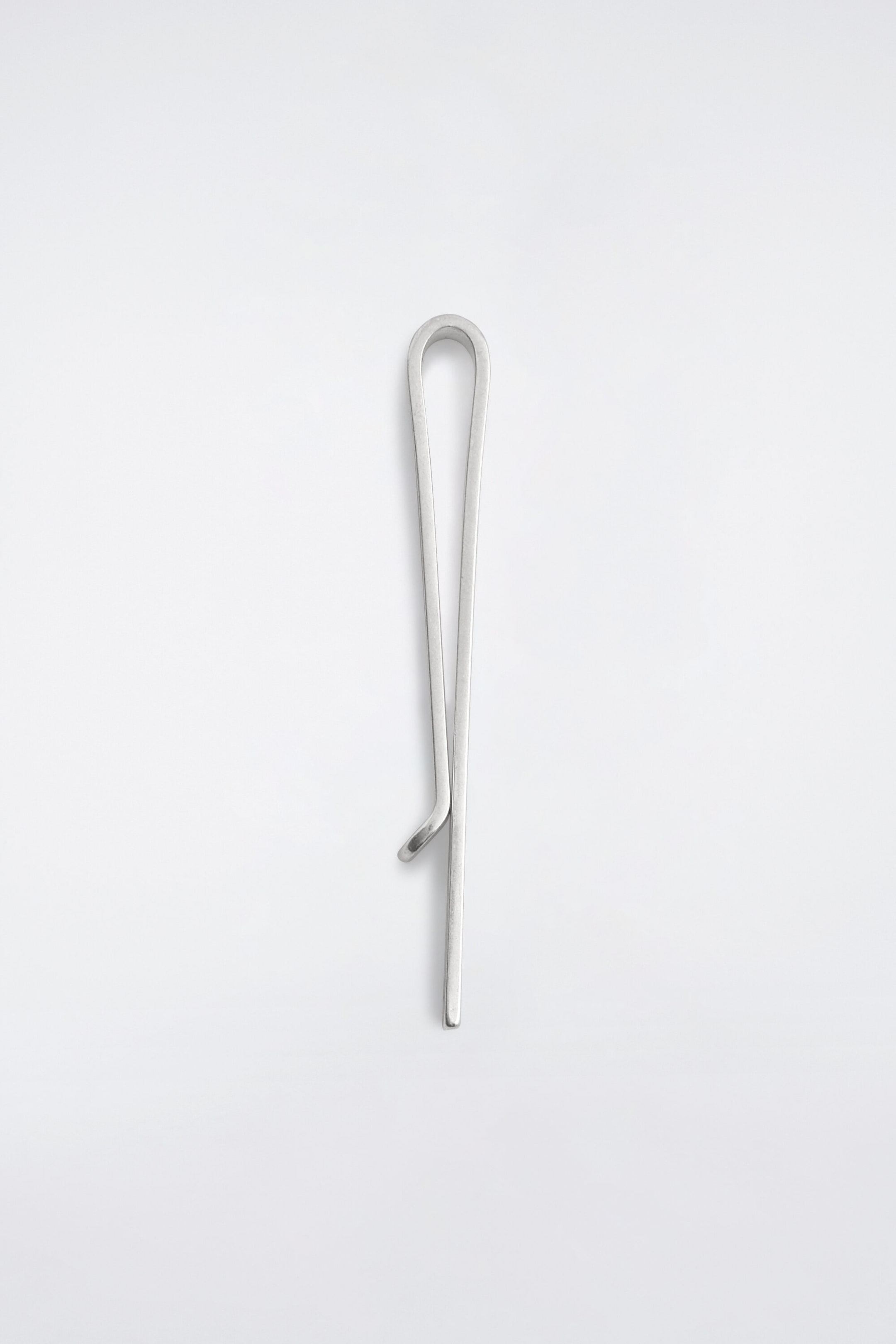 A silver-plated brass tie pin is shown from the front, showcasing its minimalist, streamlined design. The pin features a brushed finish on its single bent metal loop structure, which consists of one straight side and one shorter side curving slightly outwards at the tip. A silver-plated brass tie pin is shown from the front, showcasing its minimalist, streamlined design. The pin features a brushed finish on its single bent metal loop structure, which consists of one straight side and one shorter side curving slightly outwards at the tip.