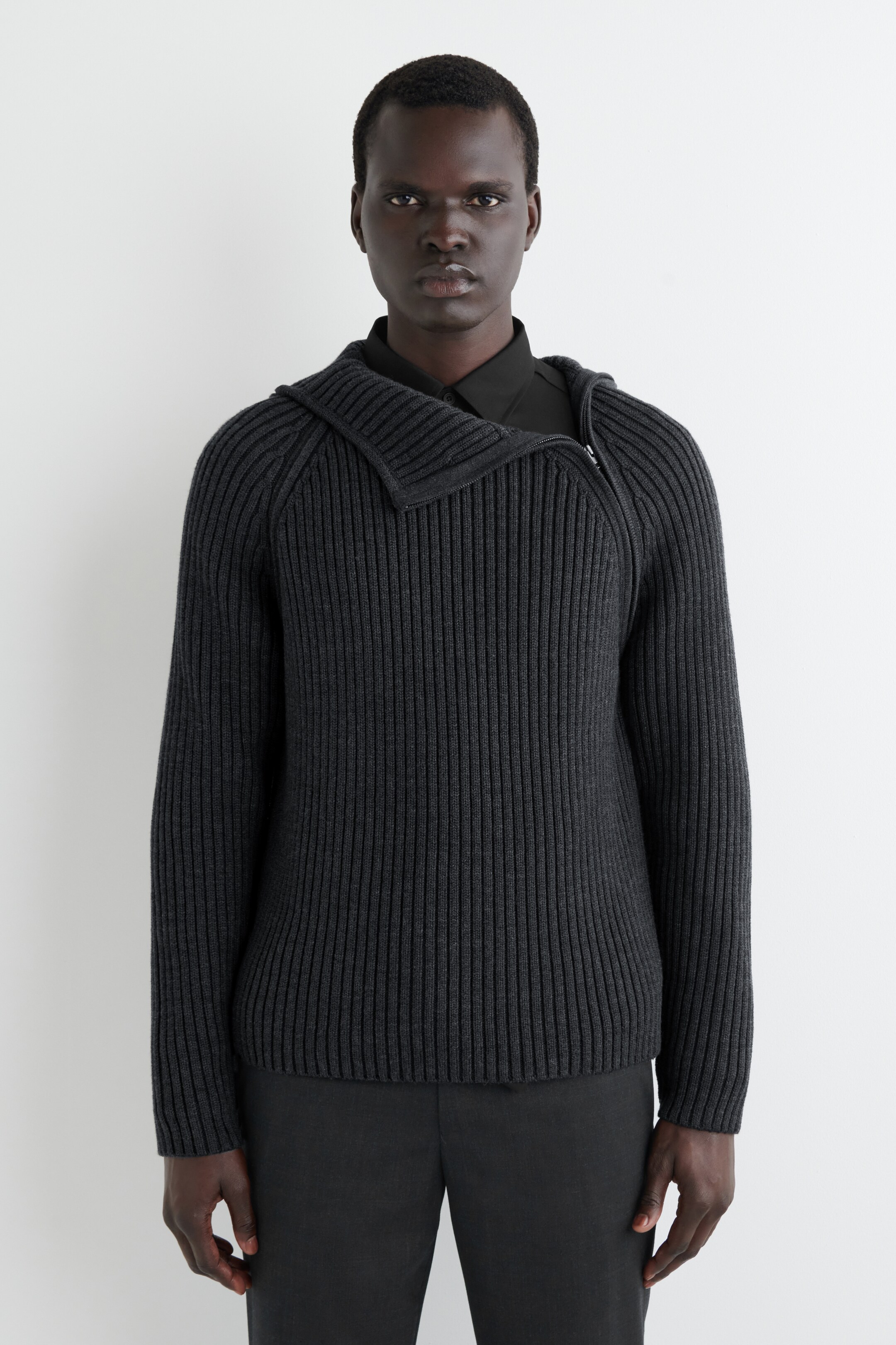 Agrandir l'image: Un pull côtelé gris foncé est présenté face avant, avec un large col montant asymétrique côtelé qui s'ouvre avec une fermeture éclair argentée sur le côté droit et est porté par-dessus une chemise noire à col.