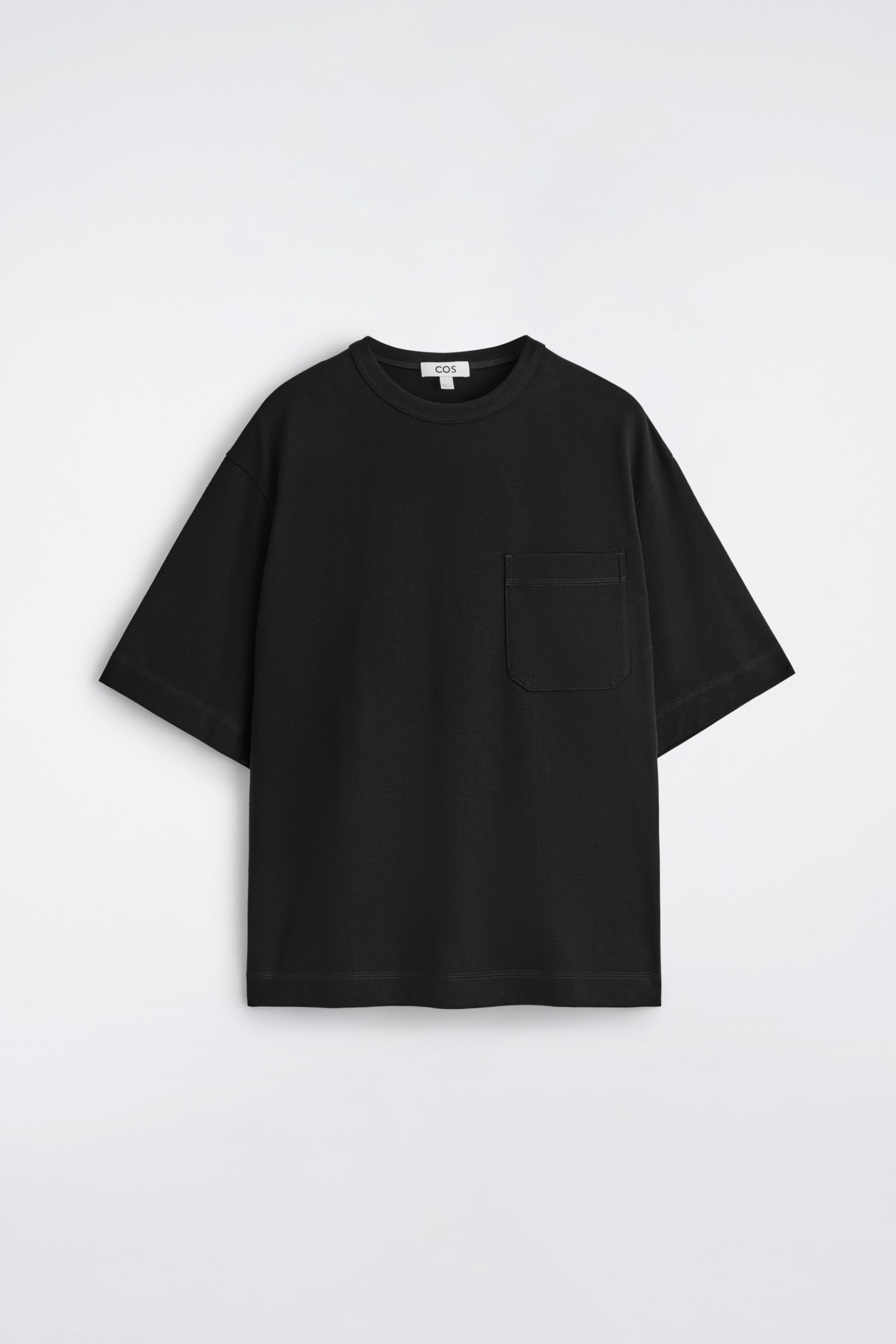 Visualizza l'immagine ingrandita: Una T-shirt nera oversize è mostrata frontalmente, caratterizzata da un collo a giro e maniche corte e larghe. Una tasca a toppa rettangolare è situata sul petto sinistro, dettagliata con cuciture visibili.