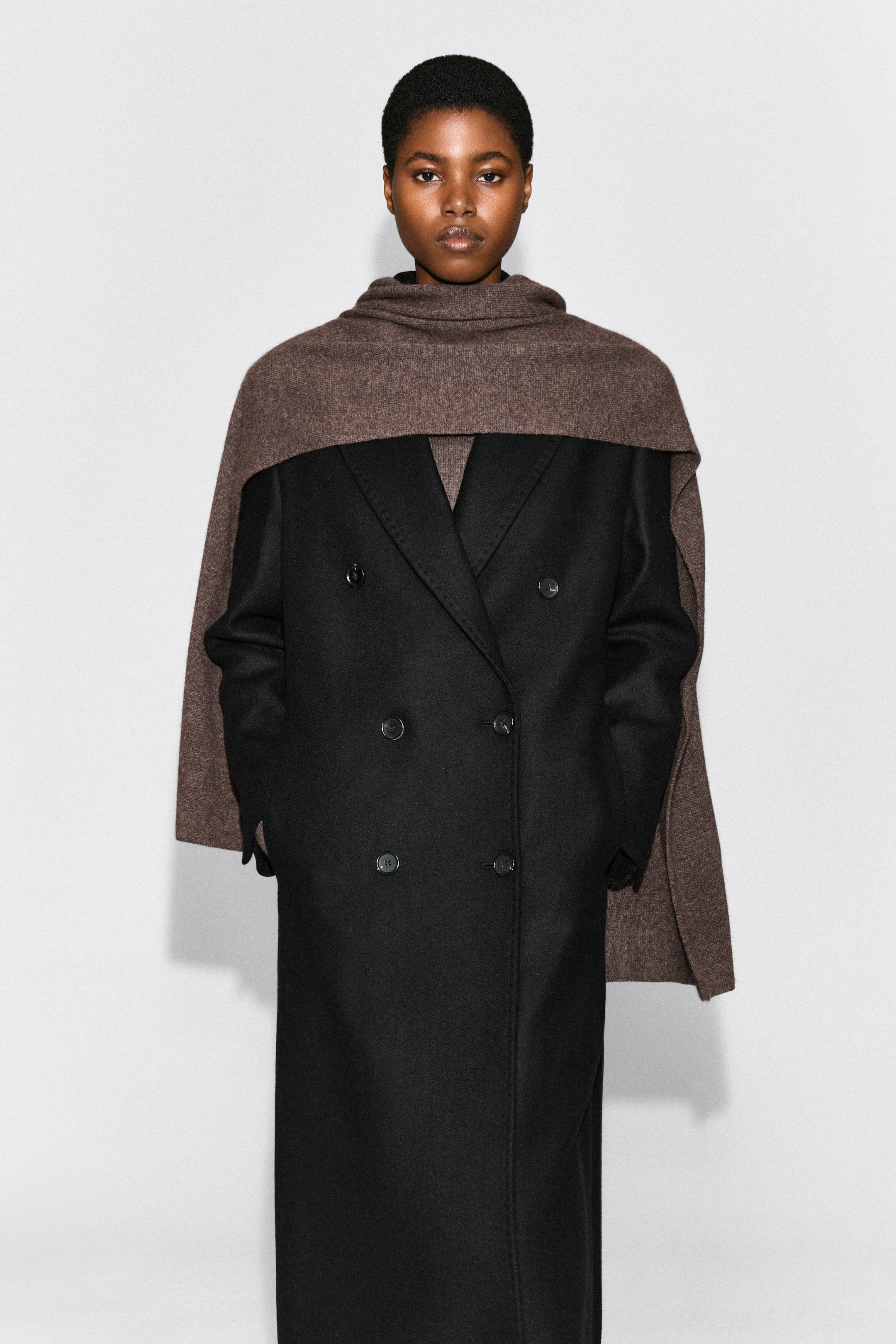 A brown cashmere scarf is being worn draped over the shoulders and wrapped around the model’s neck, layered over a black double-breasted coat. The wide scarf covers the upper chest and shoulders, with its ends hanging down the sides. A brown cashmere scarf is being worn draped over the shoulders and wrapped around the model’s neck, layered over a black double-breasted coat. The wide scarf covers the upper chest and shoulders, with its ends hanging down the sides.
