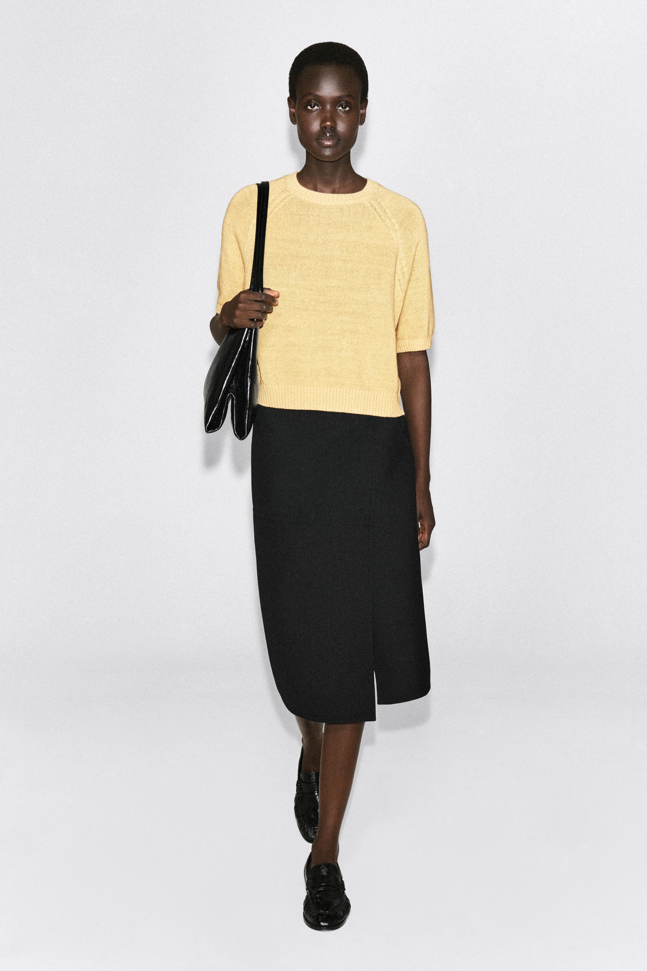 The shrunken knitted linen T-shirt in pale yellow is shown from the front, featuring a crew neck, short raglan sleeves, and ribbed trim at the collar, cuffs, and hem. The top fits close to the torso and ends in a slightly cropped length that sits just above a high-waisted black skirt. The shrunken knitted linen T-shirt in pale yellow is shown from the front, featuring a crew neck, short raglan sleeves, and ribbed trim at the collar, cuffs, and hem. The top fits close to the torso and ends in a slightly cropped length that sits just above a high-waisted black skirt.