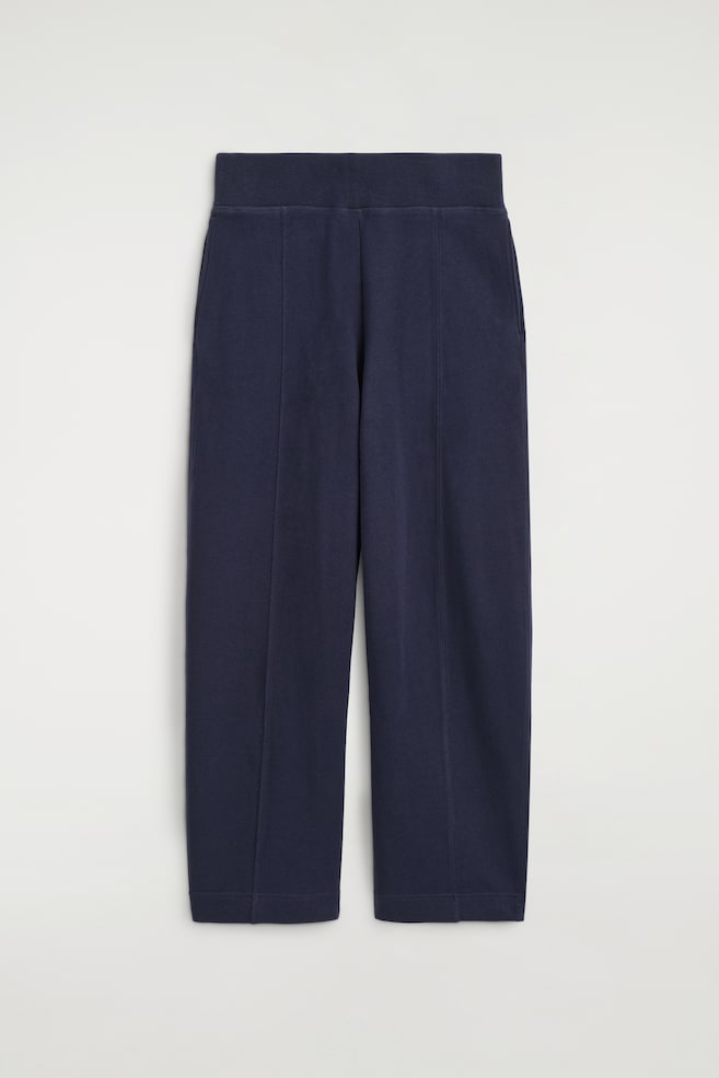 Diese marineblauen Jogger aus Baumwolle sind von vorne zu sehen und verfÃ¼gen Ã¼ber einen breiten elastischen Bund sowie vertikale MittelnahtverlÃ¤ufe an beiden Beinen. Die Hose zeigt eine strukturierte, geschwungene Barrel-Leg-Silhouette, die sich zum Saum hin leicht verjÃ¼ngt. - 1
