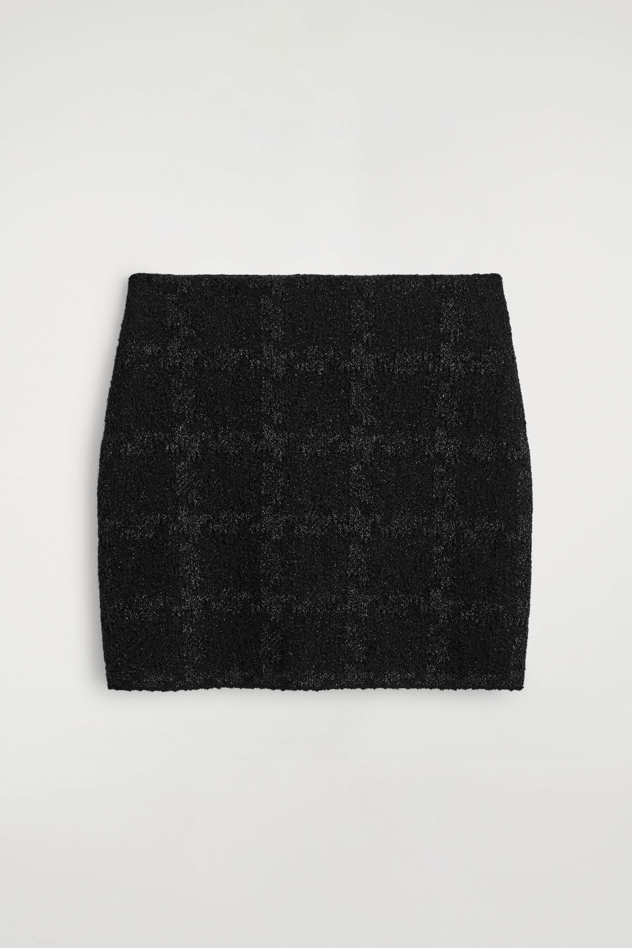 Grotere afbeelding bekijken: De voorkant van een zwarte minirok toont een subtiel ruitpatroon, vervaardigd uit een tactiele bouclé breisel met metallic draden.