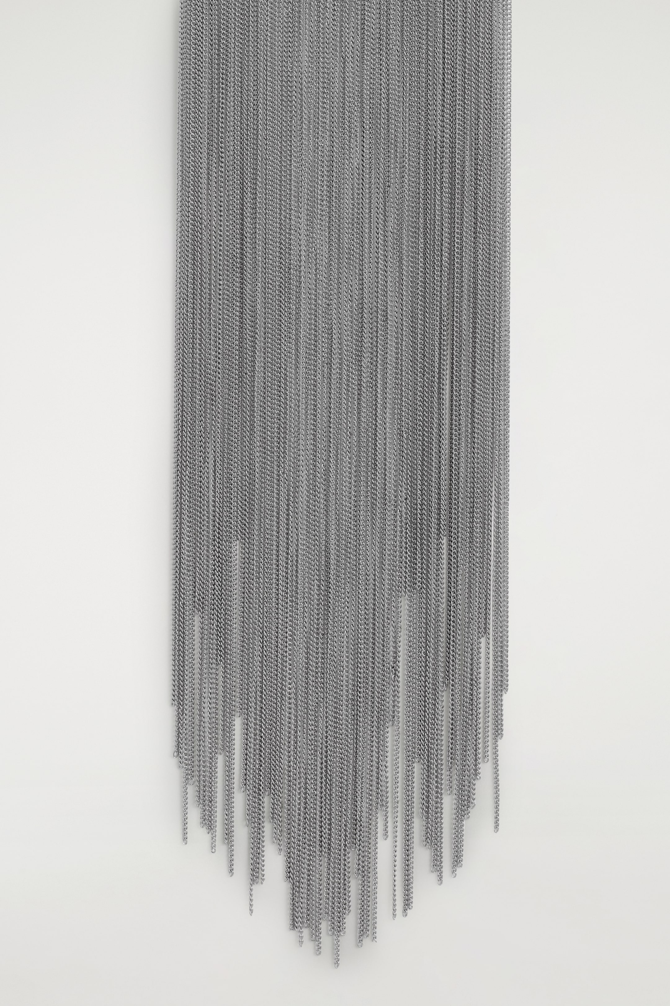 View larger image: The FRONT of a silver-colored necklace is featuring elongated tasselled chains that are cascading downwards from a slim chain. The numerous individual chains are forming a dense, layered mass that is creating an uneven, pointed shape at the bottom.