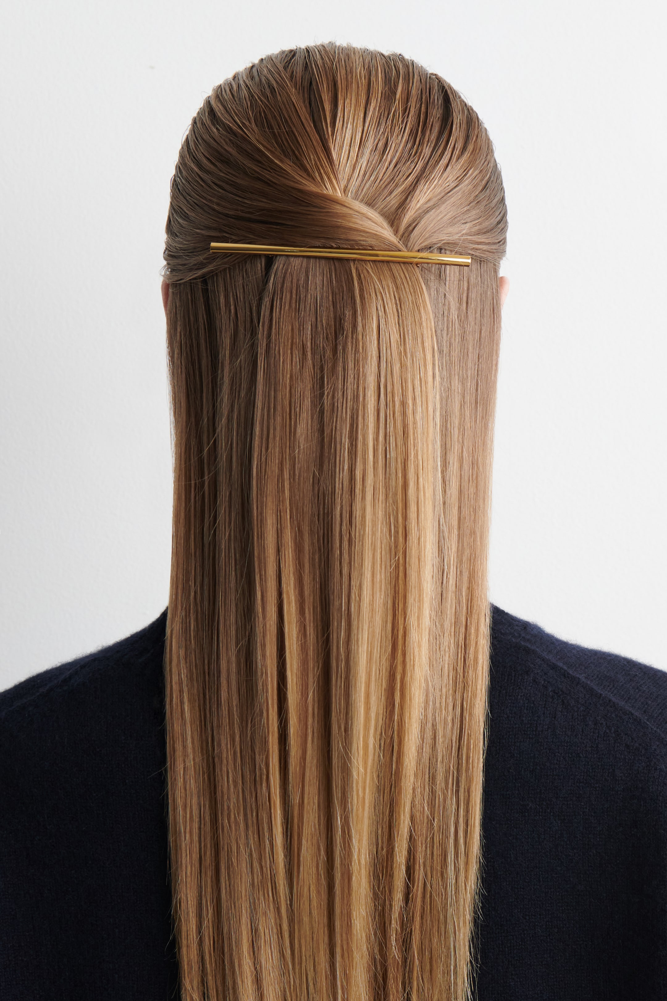 Visualizza immagine più grande: Una forcina lineare, lucida e dorata sta fissando una sezione dei lunghi capelli castano chiaro della modella, che sono acconciati in un mezzo raccolto intrecciato.