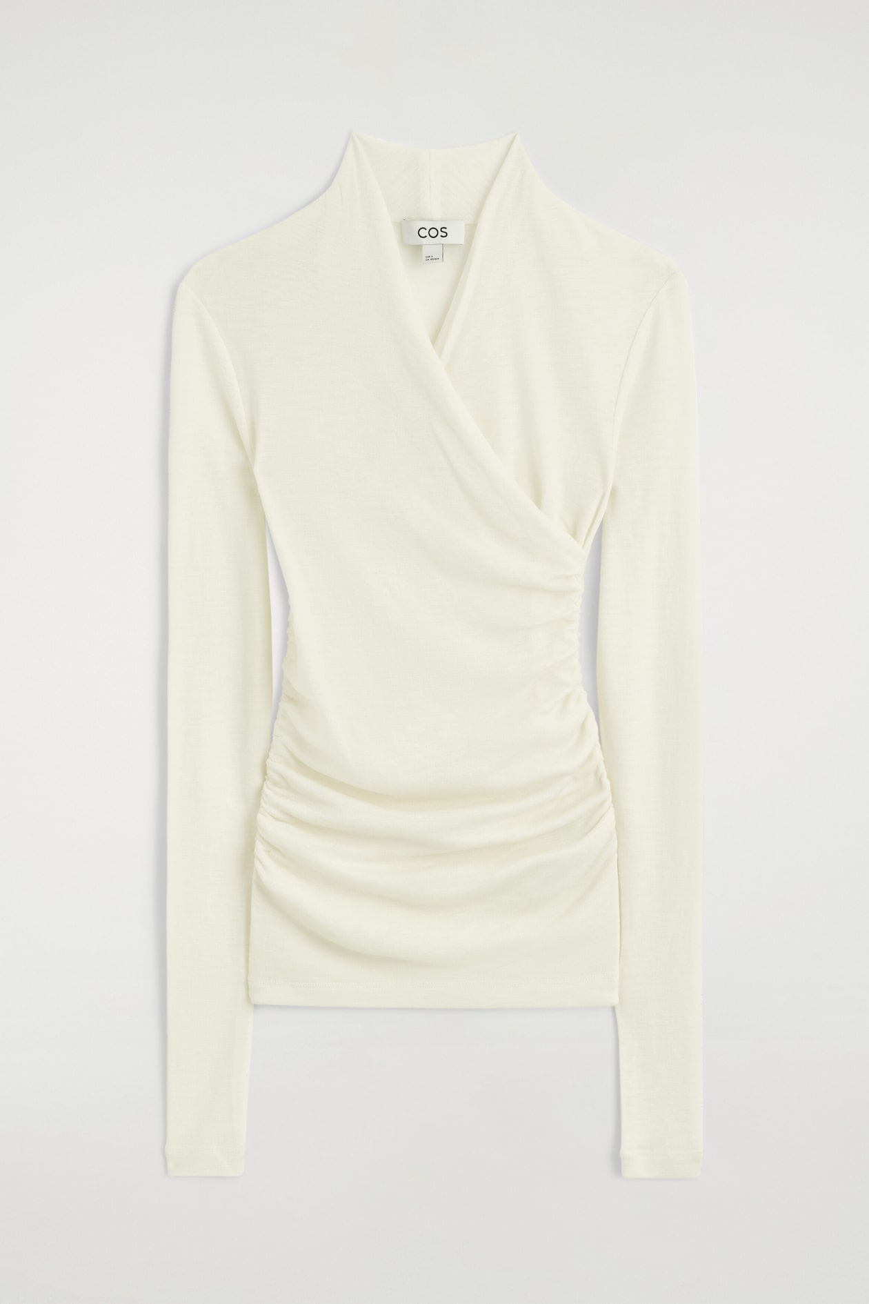 An off-white, long-sleeve top is shown from the front, featuring a wrap-front design with a shawl collar. The slim-fit top has gathered detailing along the sides, creating draping across the front.