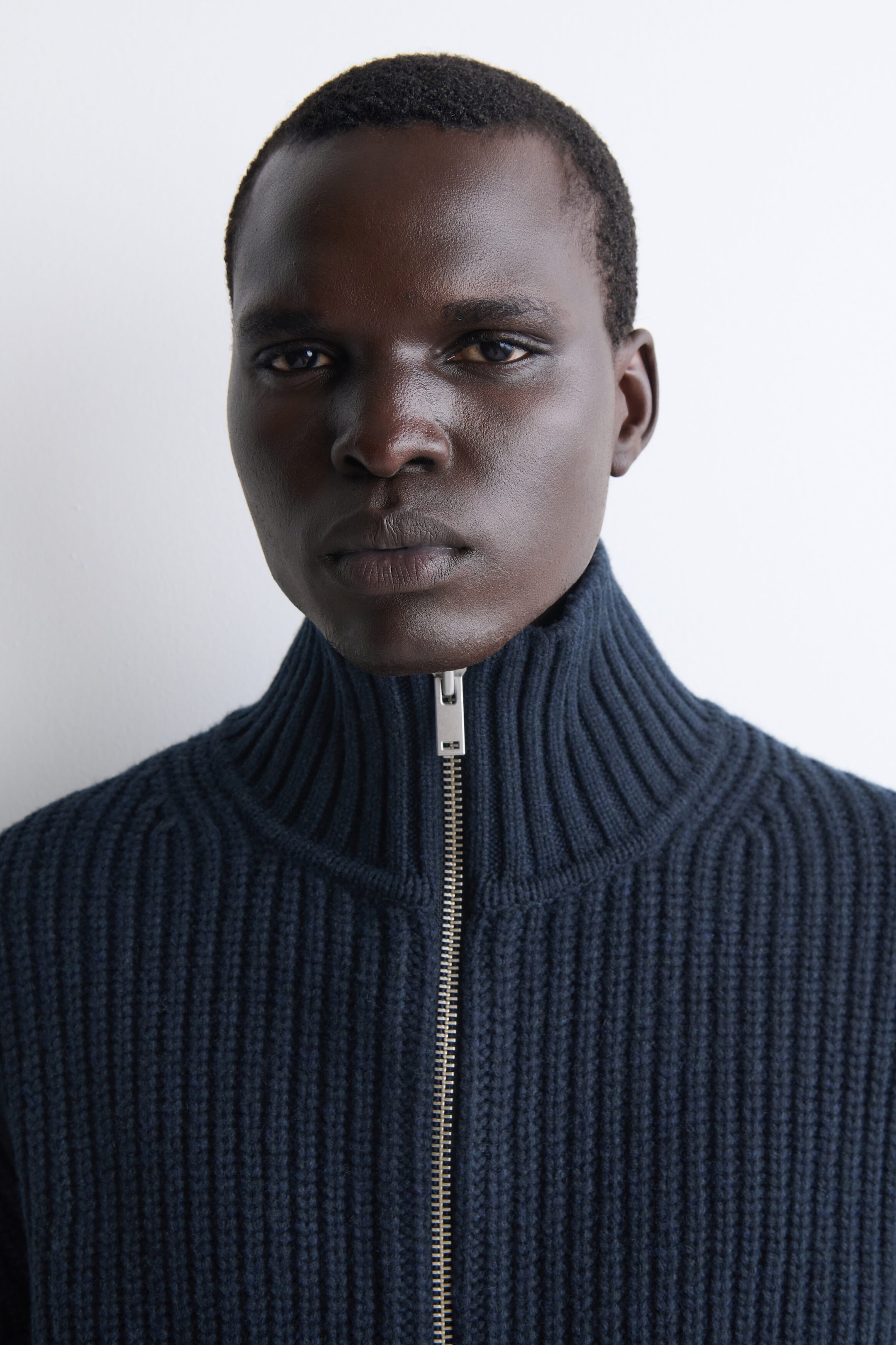 A navy blue ribbed-knit sweater features a high funnel neck and a silver-toned front zipper. The garment showcases a thick, vertical rib-knit pattern throughout. A navy blue ribbed-knit sweater features a high funnel neck and a silver-toned front zipper. The garment showcases a thick, vertical rib-knit pattern throughout.