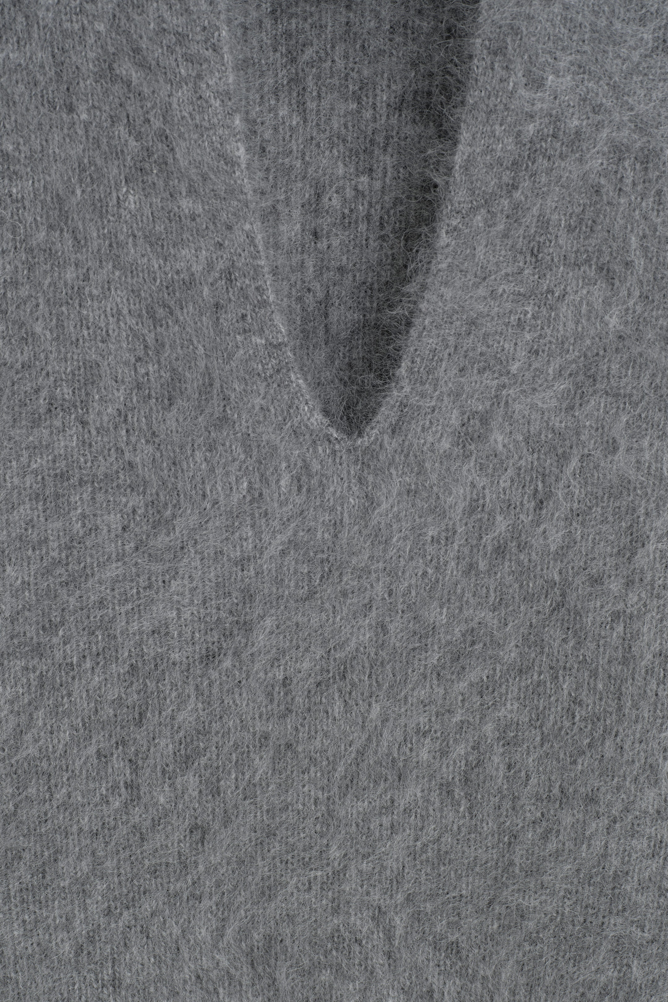 Un gros plan met en valeur la texture douce et brossée de la laine du haut tricoté gris, ainsi que la base de son col en V incurvé. Un gros plan met en valeur la texture douce et brossée de la laine du haut tricoté gris, ainsi que la base de son col en V incurvé.