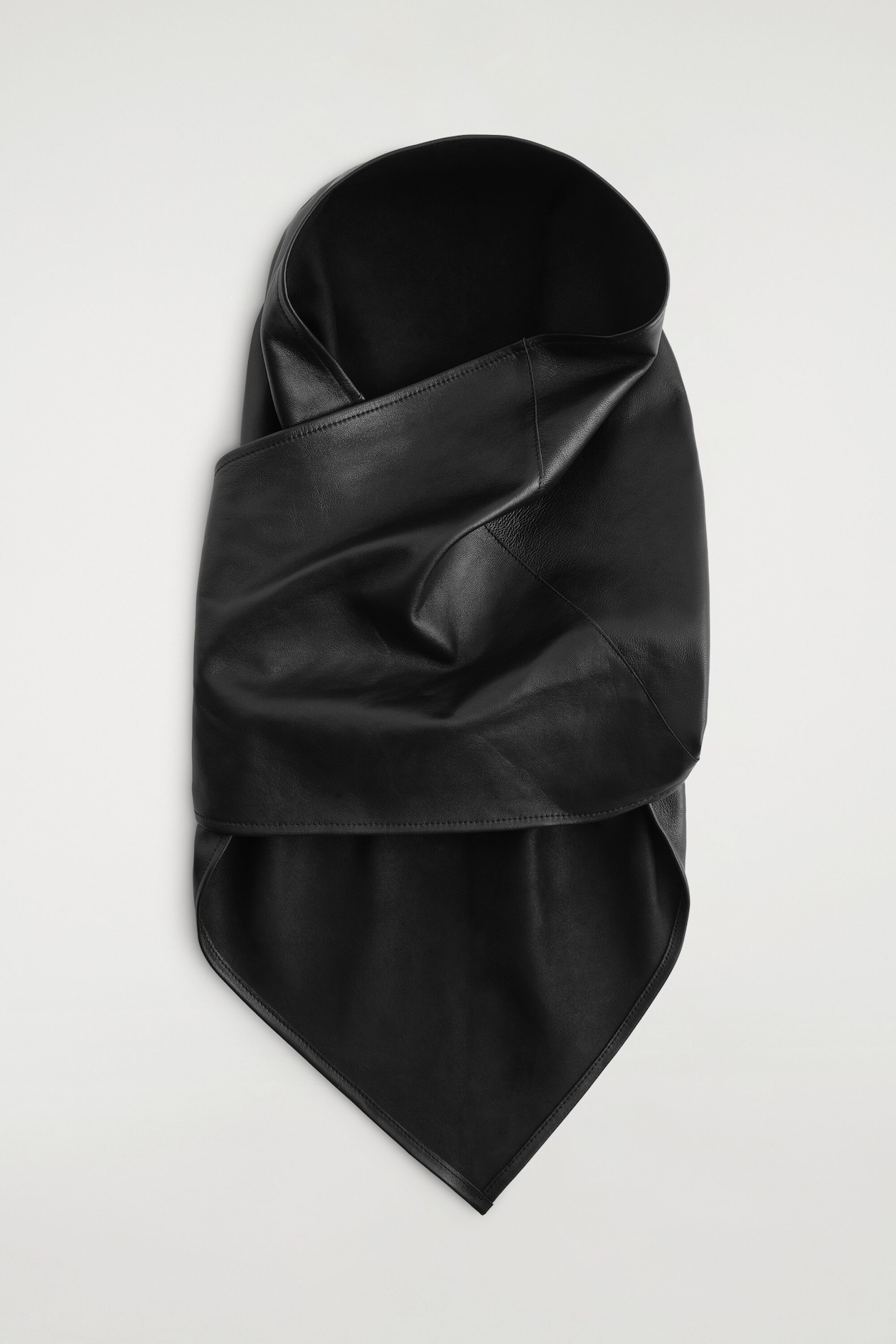 The leather hood, shown from the front, features a draped, wrapped design crafted from smooth black leather. It showcases a structured hood opening at the top, overlapping folds across the centre, and a pointed triangular bib draping at the bottom.