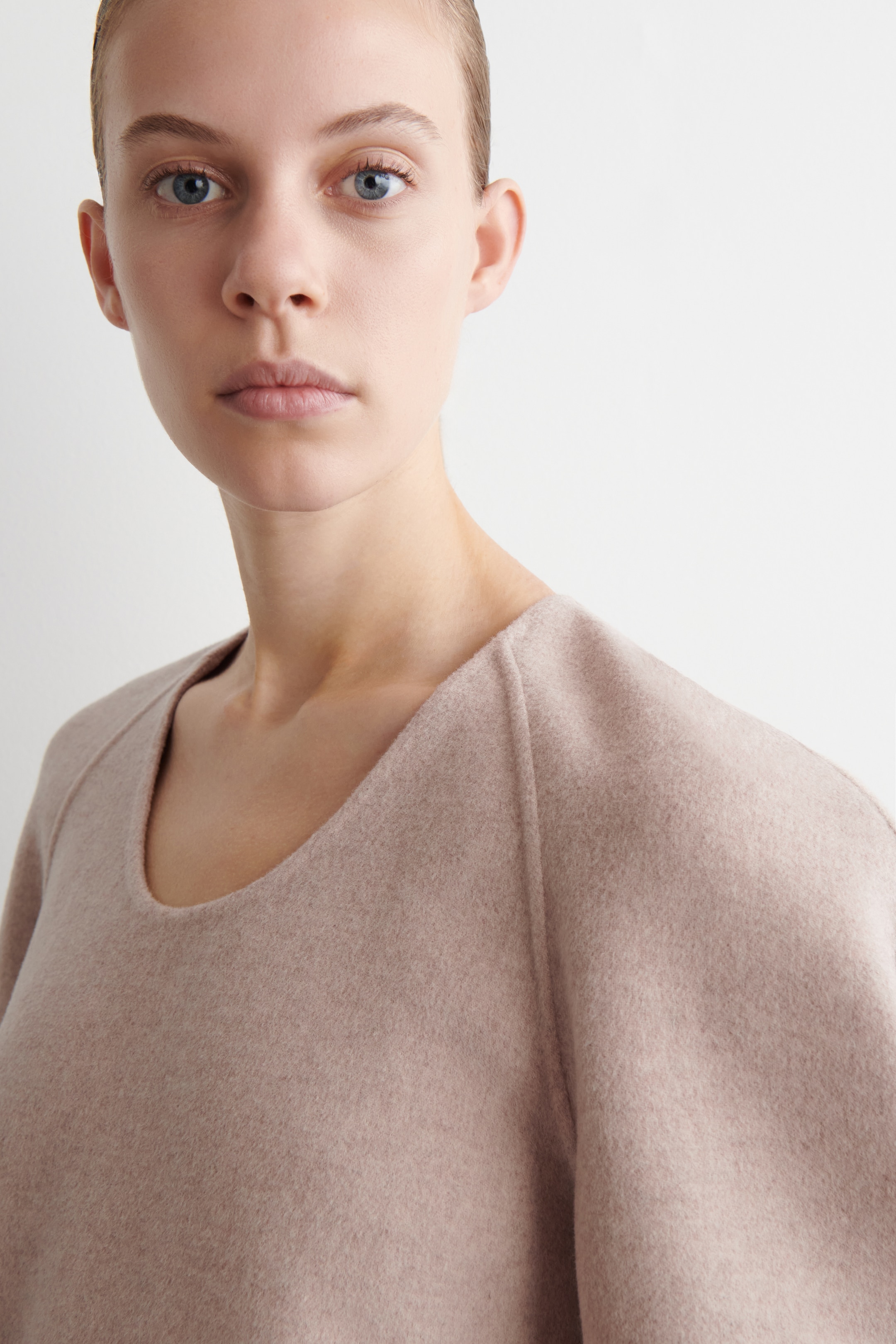View larger image: A light pink top is featuring a wide scoop neck and raglan sleeves. The soft, brushed material is draping loosely, with the garment angled to the right to showcase its relaxed fit.