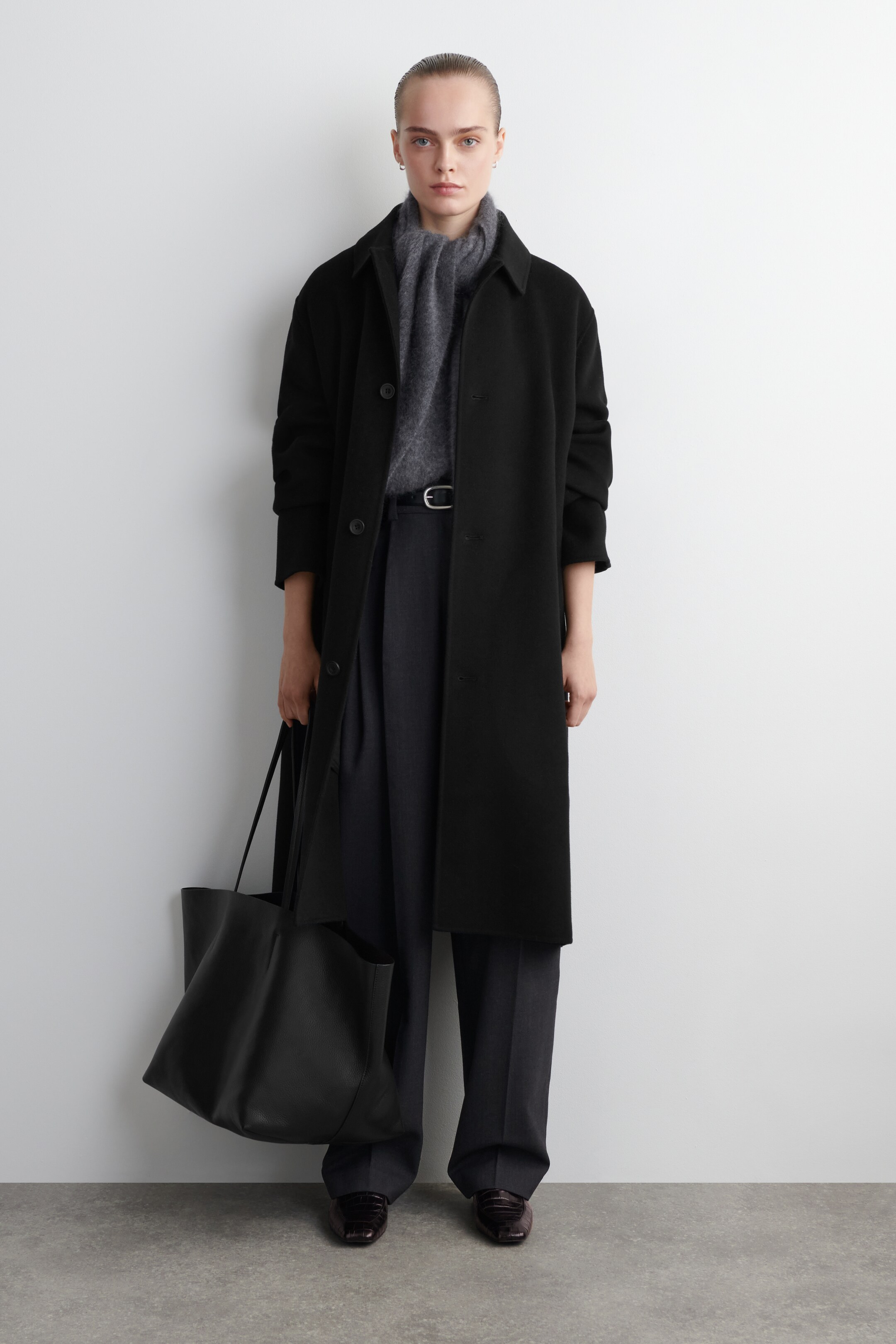 Agrandir l'image: Un sac fourre-tout en cuir noir est porté, présentant sa vue de face. Il présente une texture légèrement grainée, un dessus ouvert et deux fines lanières.
