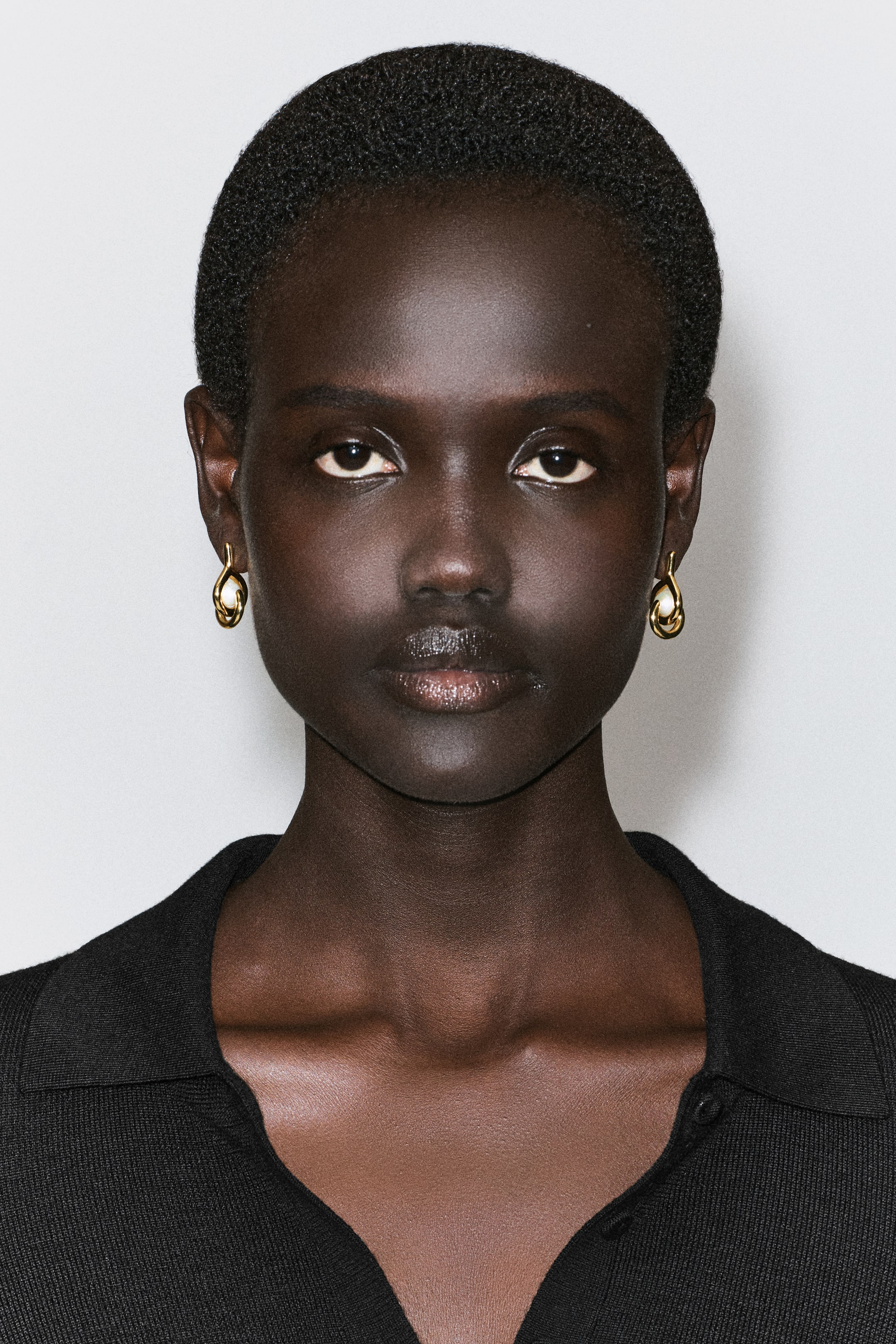 View larger image: Sculptural pearl earrings are being worn facing forwards, featuring a fluid, twisted gold-toned metal loop cradling a single white pearl nestled inside.